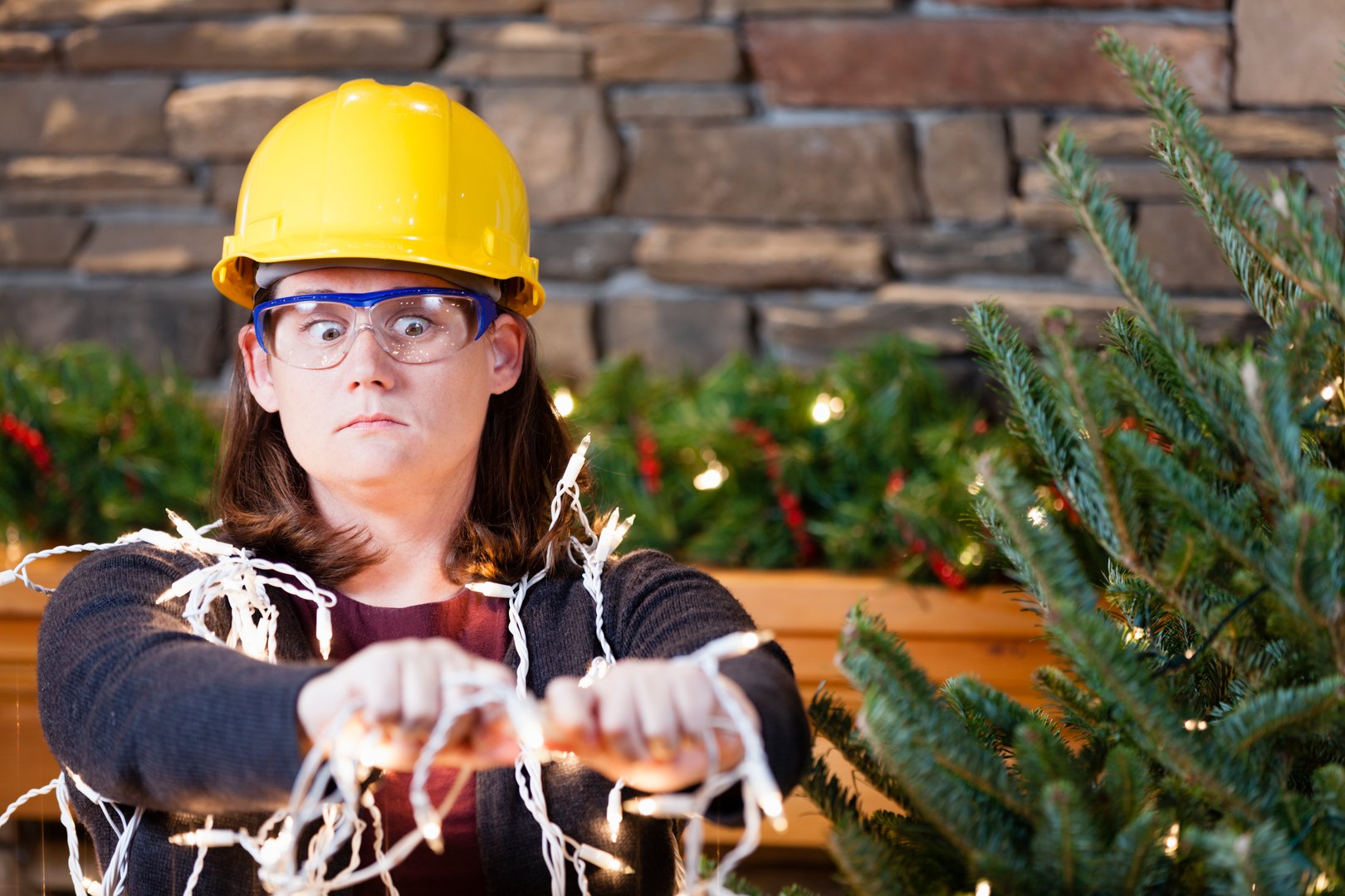 Young woman wearing hardhat and safety glasses plugging in Christmas tree lights