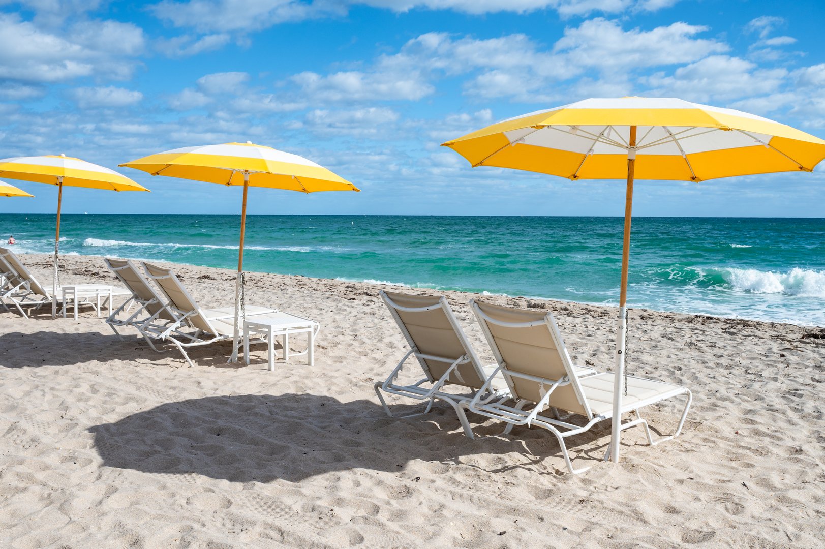Luxury beach chairs and yellow umbrellas on white sand at the sea in Fort Lauderdale, Florida. No people.