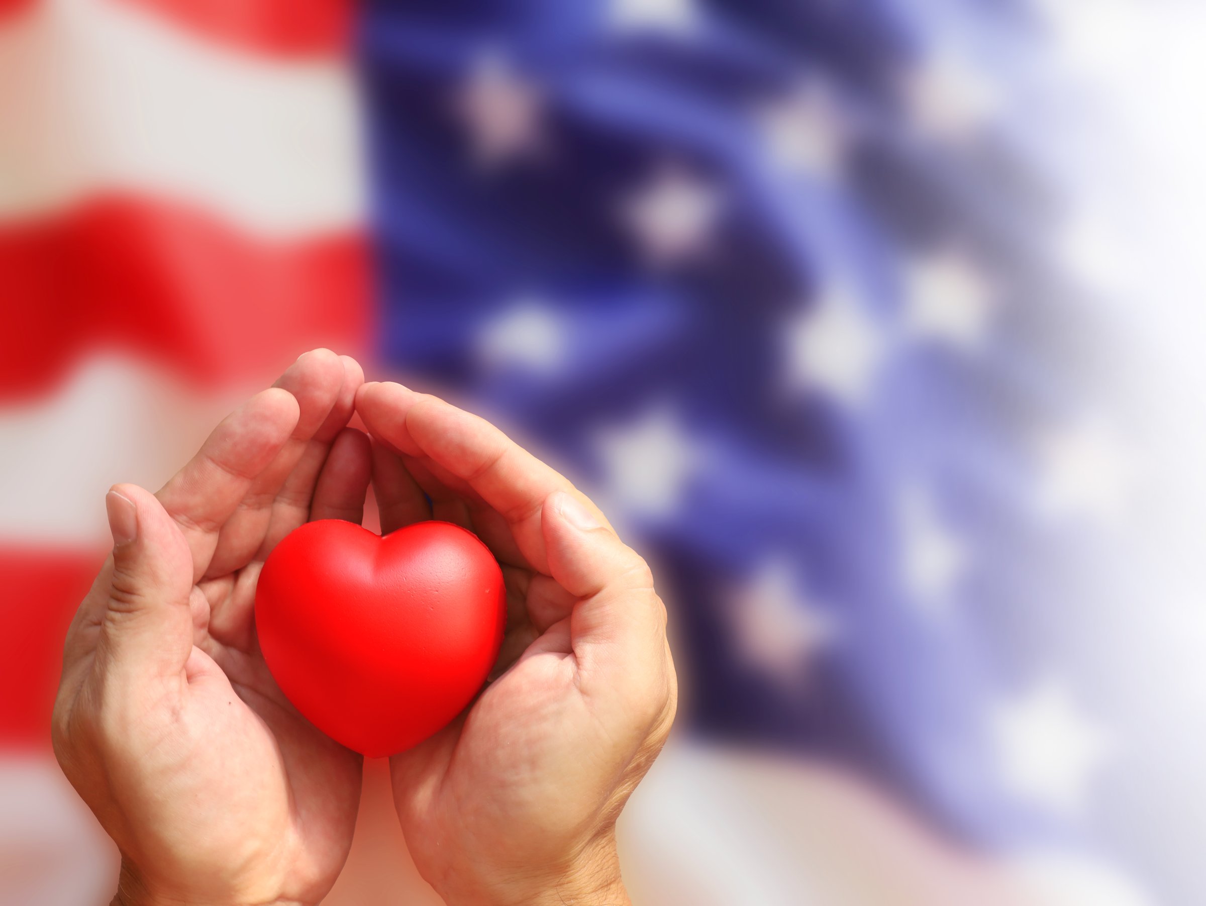 Red heart in the hands on US flag background.