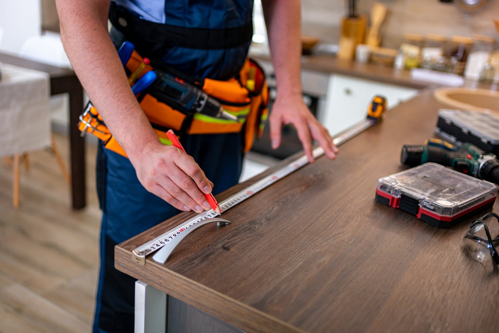 Worker uses measuring tape and pencil to mark countertop dimensions in modern kitchen design
