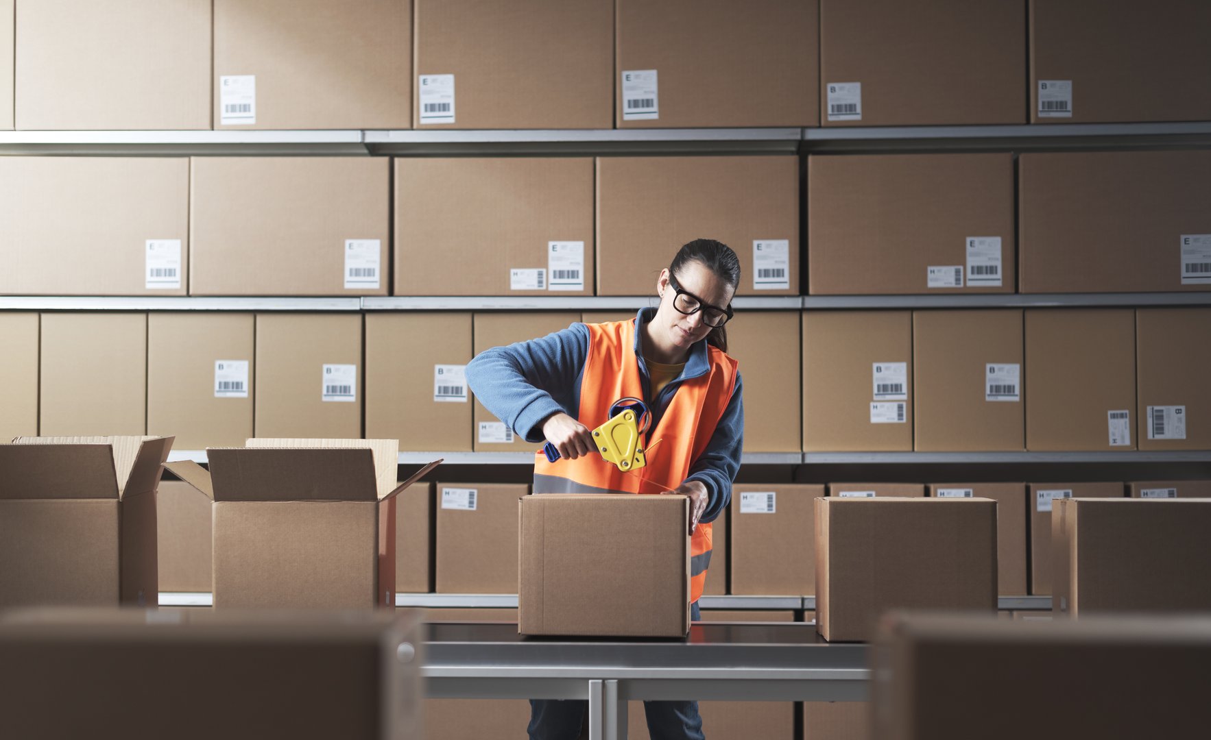 Bored warehouse worker sealing boxes on the conveyor belt with adhesive tape