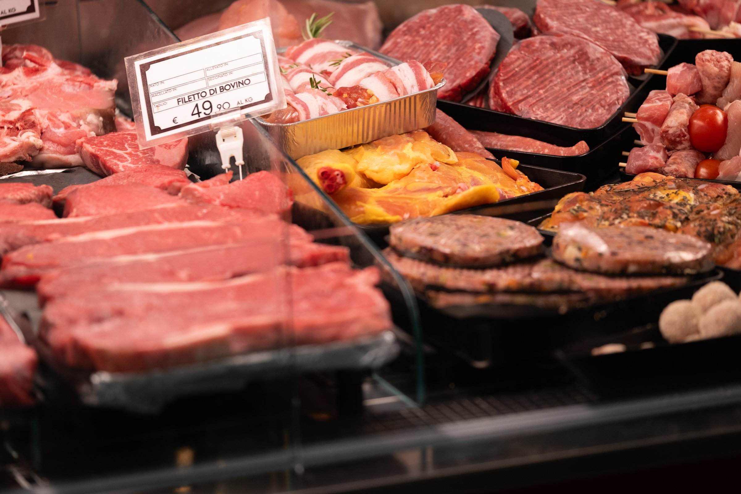 Close-up view of a meat counter filled with various fresh cuts, including beef fillet, steaks, skewers, seasoned burgers, and marinated meat. Ideal for use in food, retail, or culinary publications.
