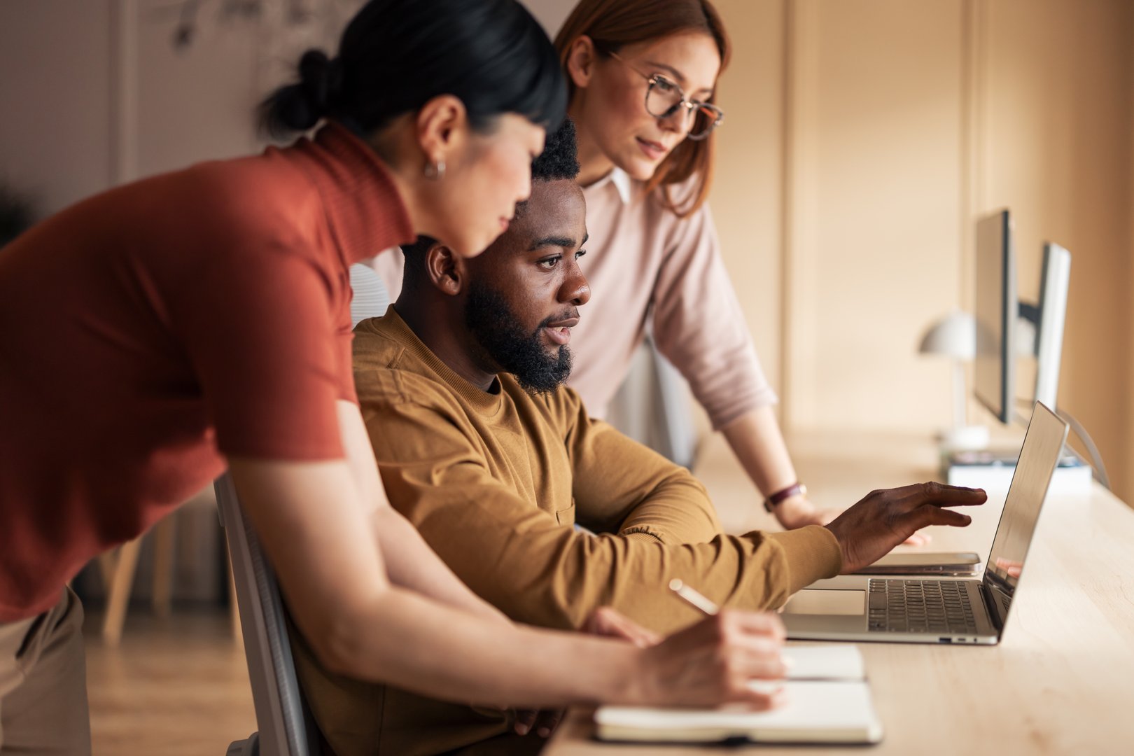A team of professionals working collaboratively at a desk, utilizing a laptop for a shared project in a modern office.