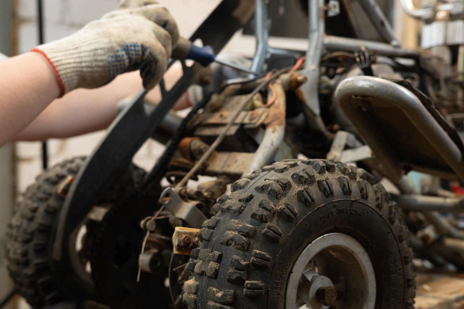 A male mechanic replaces a broken part in his son's ATV with a new one using tools. A man is repairing a small children's ATV in a garage near his house. ATV repair concept.