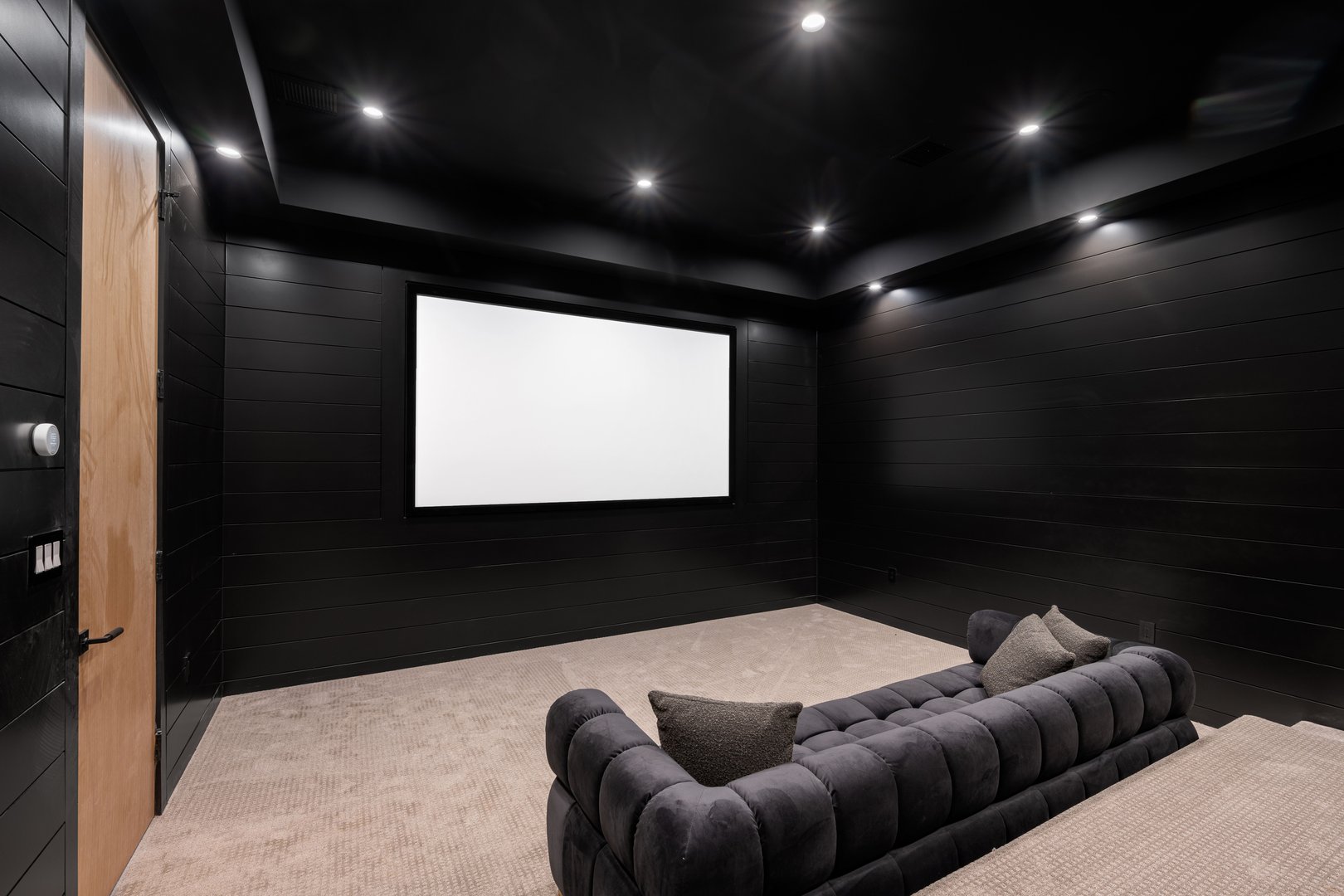 Modern home theater room with black walls, large screen, and comfortable seating.