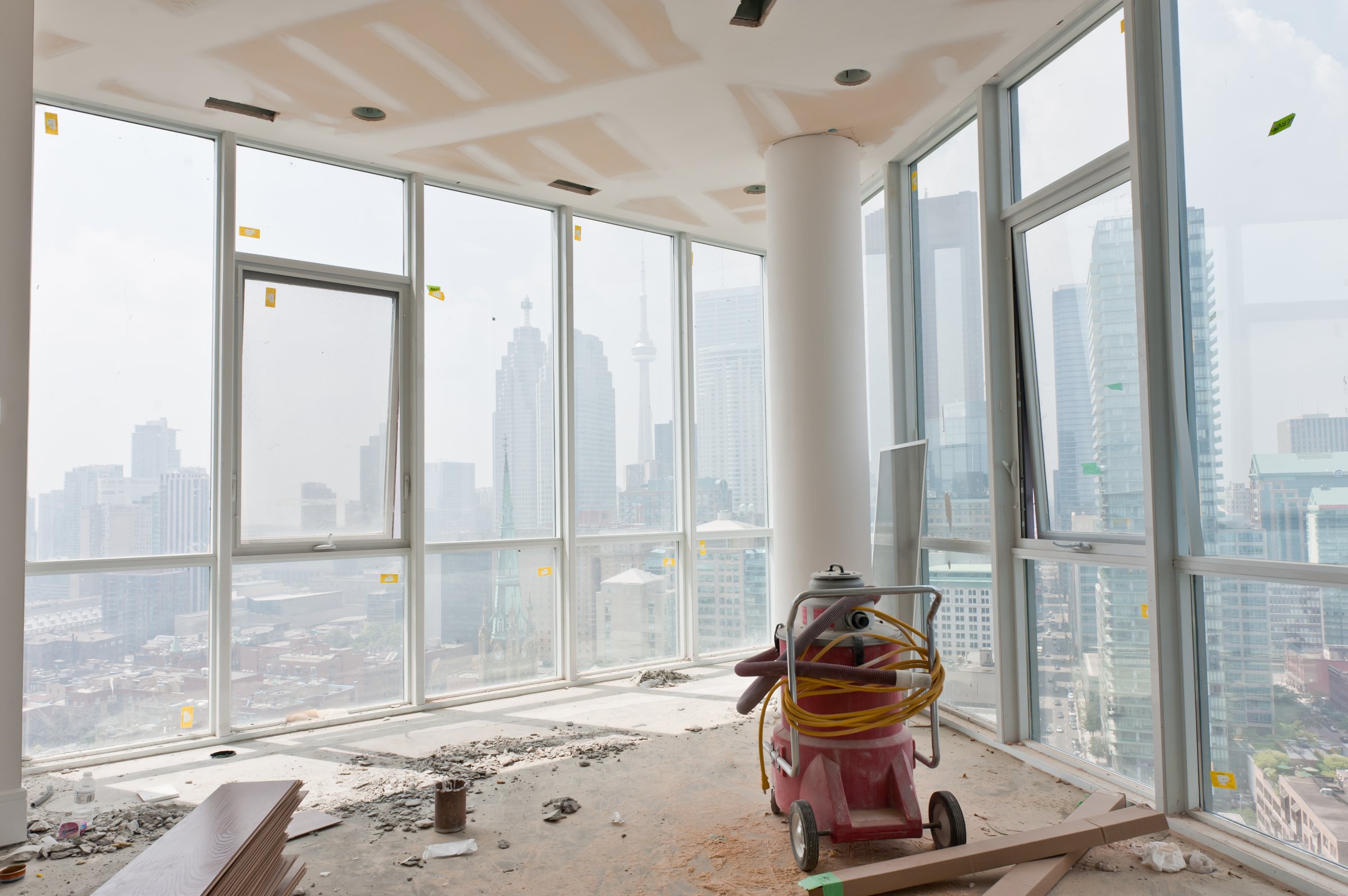 Appartamento in costruzione con grandi finestre e vista sulla città, con attrezzi e materiali da costruzione sul pavimento.