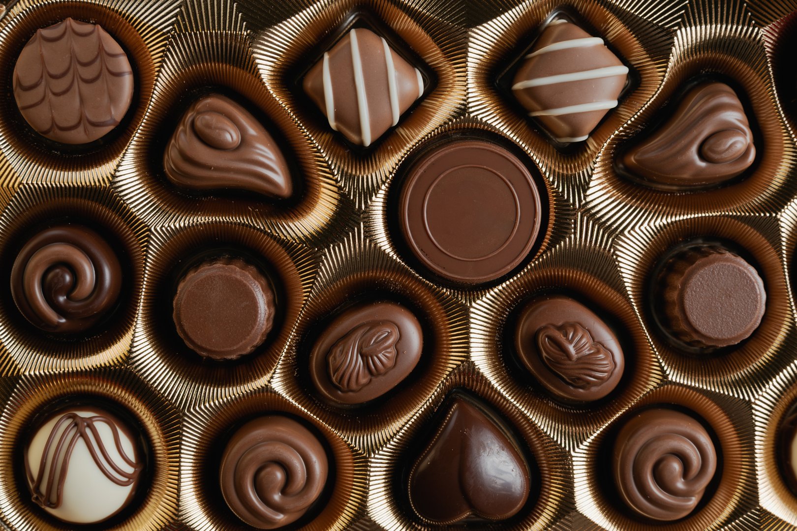 An overhead view of a luxurious gold box filled with an assortment of various milk and dark chocolates