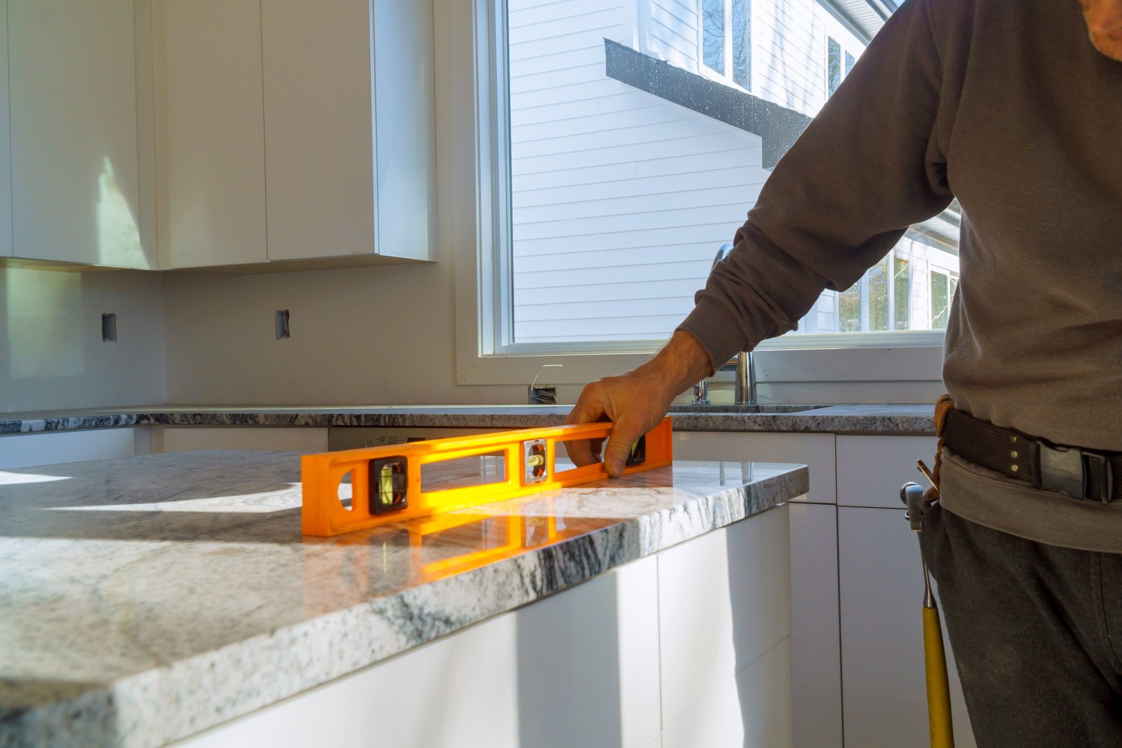 Under construction with worker checks the leveling of a granite slab for use in a home kitchen remodel