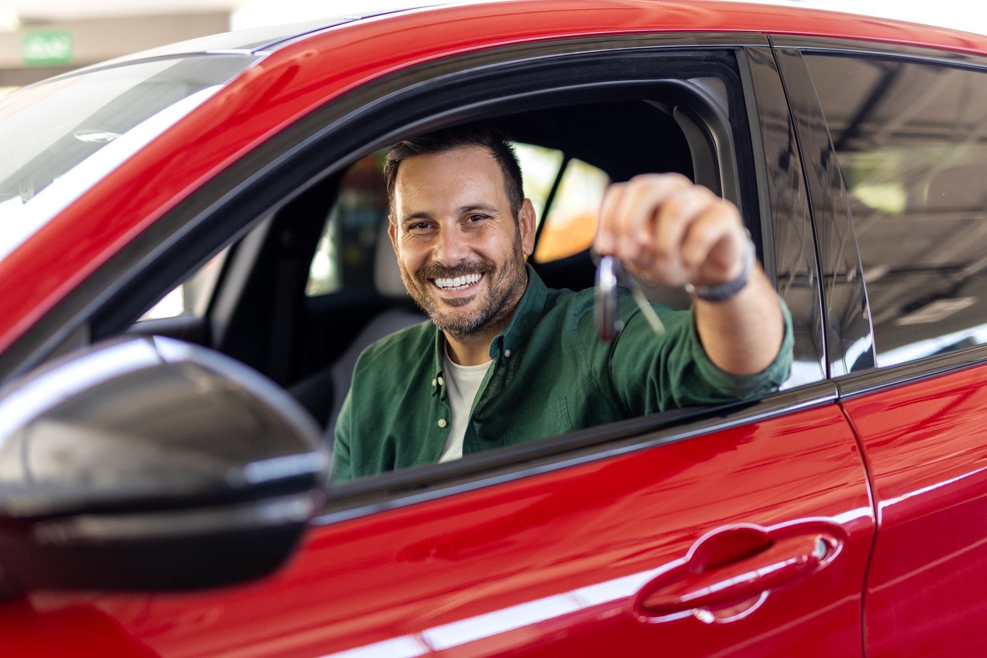 Handsome man raising hand up with the car key and smiling at camera, showing key from his brand new car, copy space. Man buying auto at luxury dealership salon