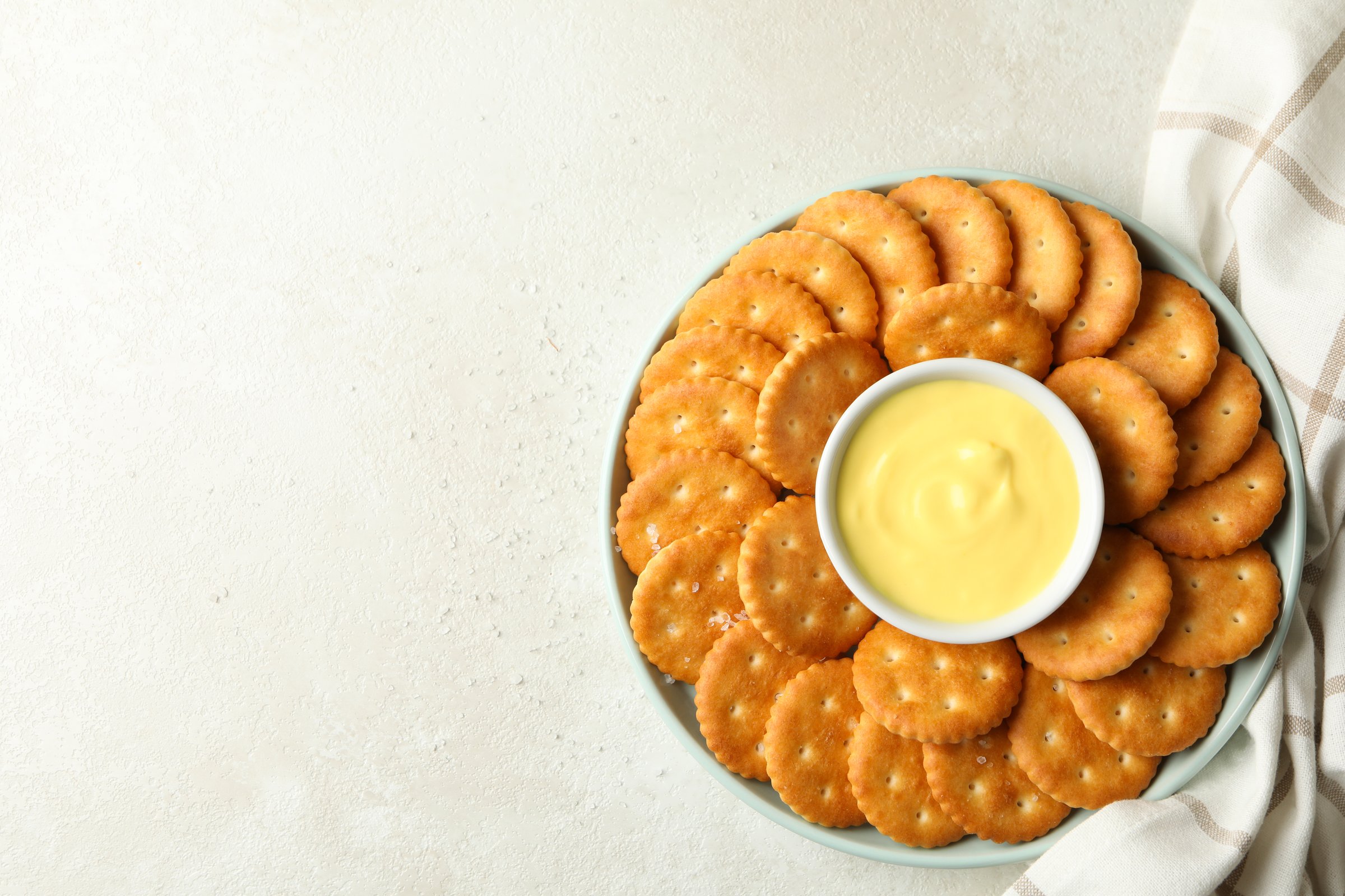 Napkin and plate with cracker biscuits and cheese sauce on white - light beige background