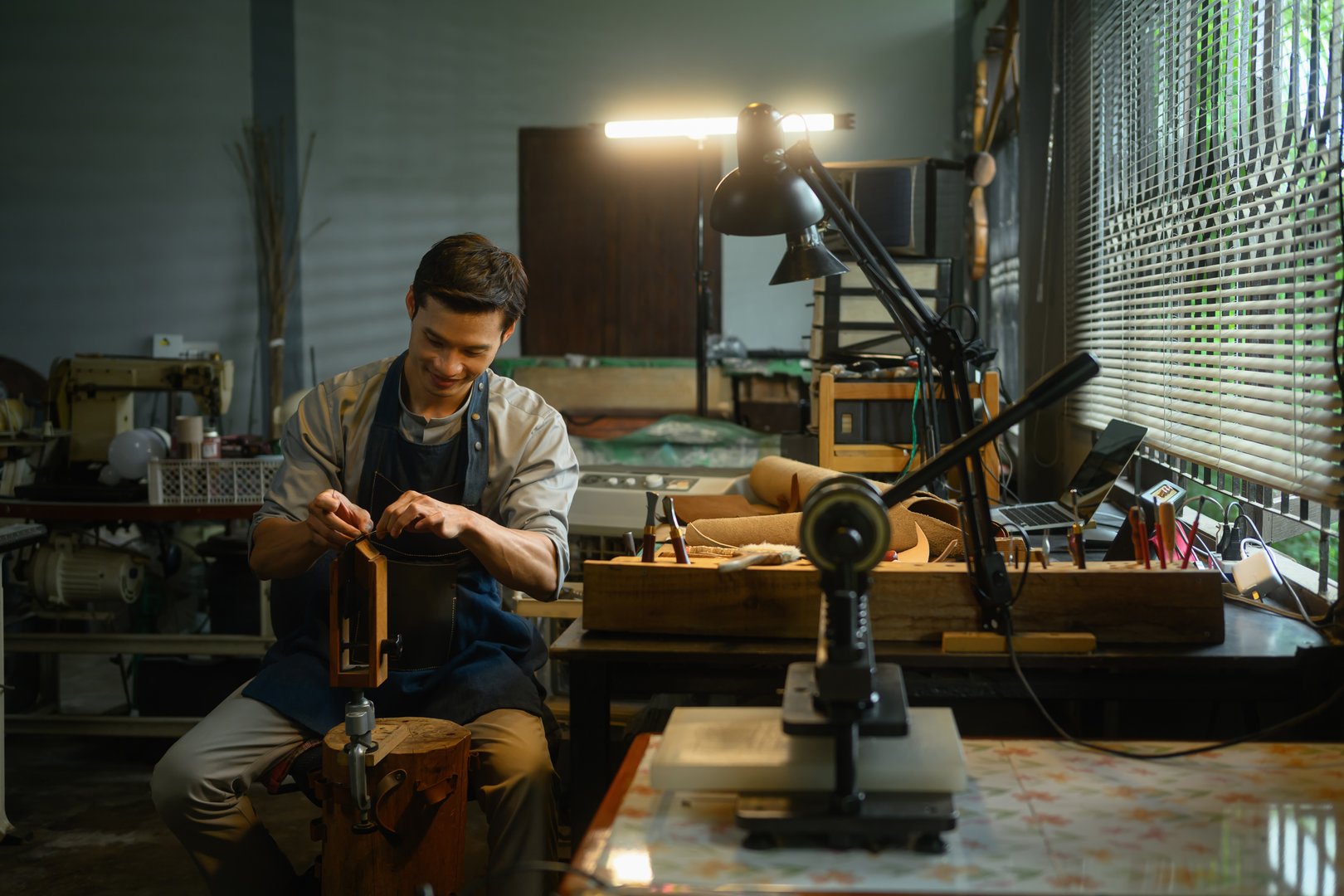 Craftsman creating product sewing leather with needle and thread in workshop.