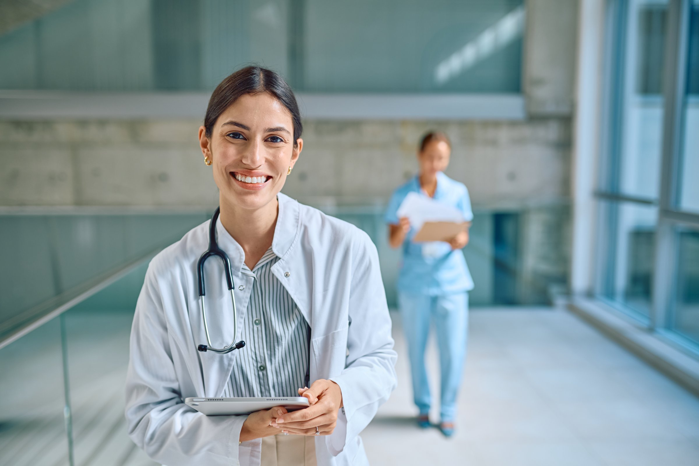 Médica femenina sonriente con estetoscopio y tablet en clínica moderna