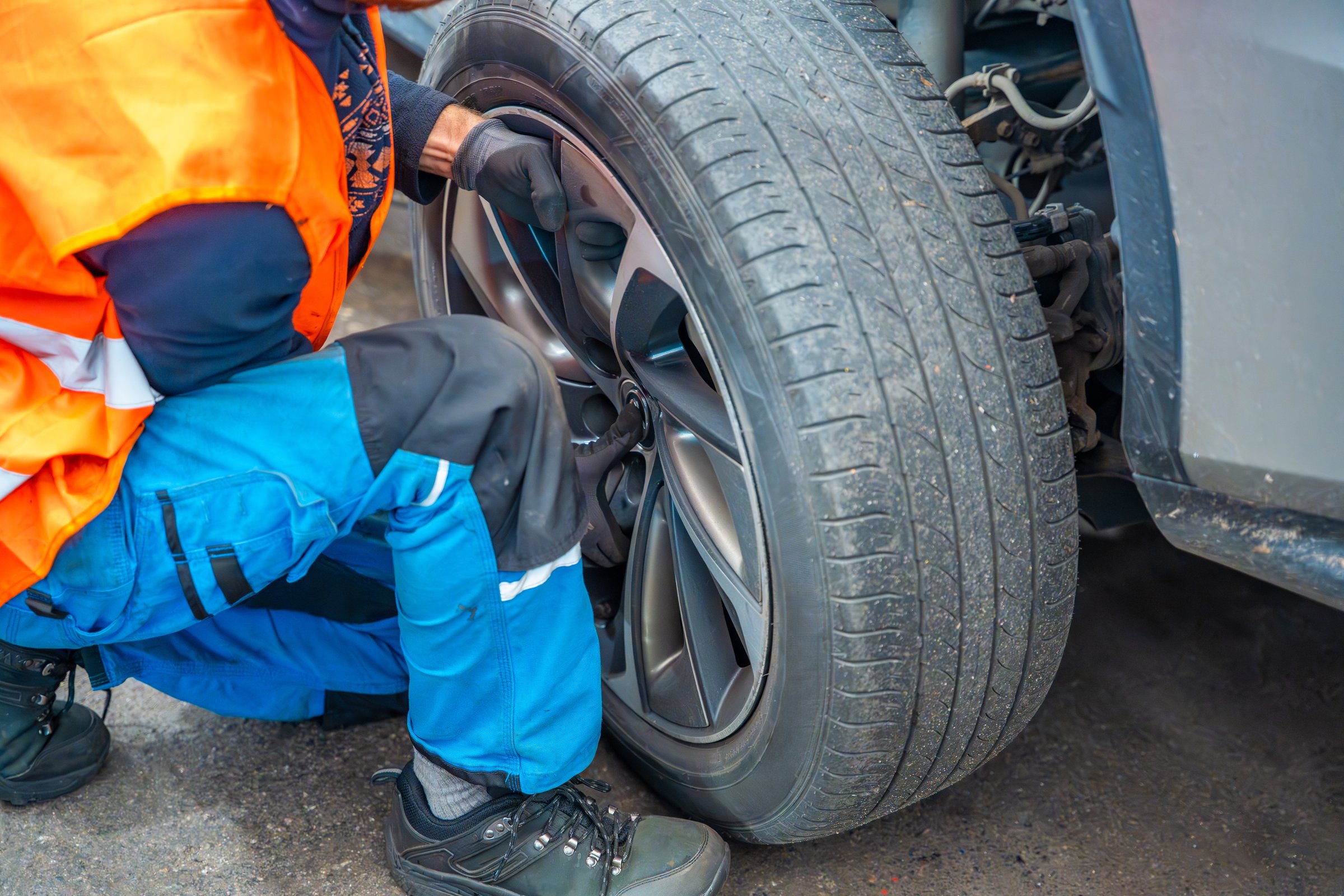 Mechanic removing a car wheel during seasonal tire change at an auto service shop. Timely winter tire replacement ensures road safety and compliance with regulations. High quality photo