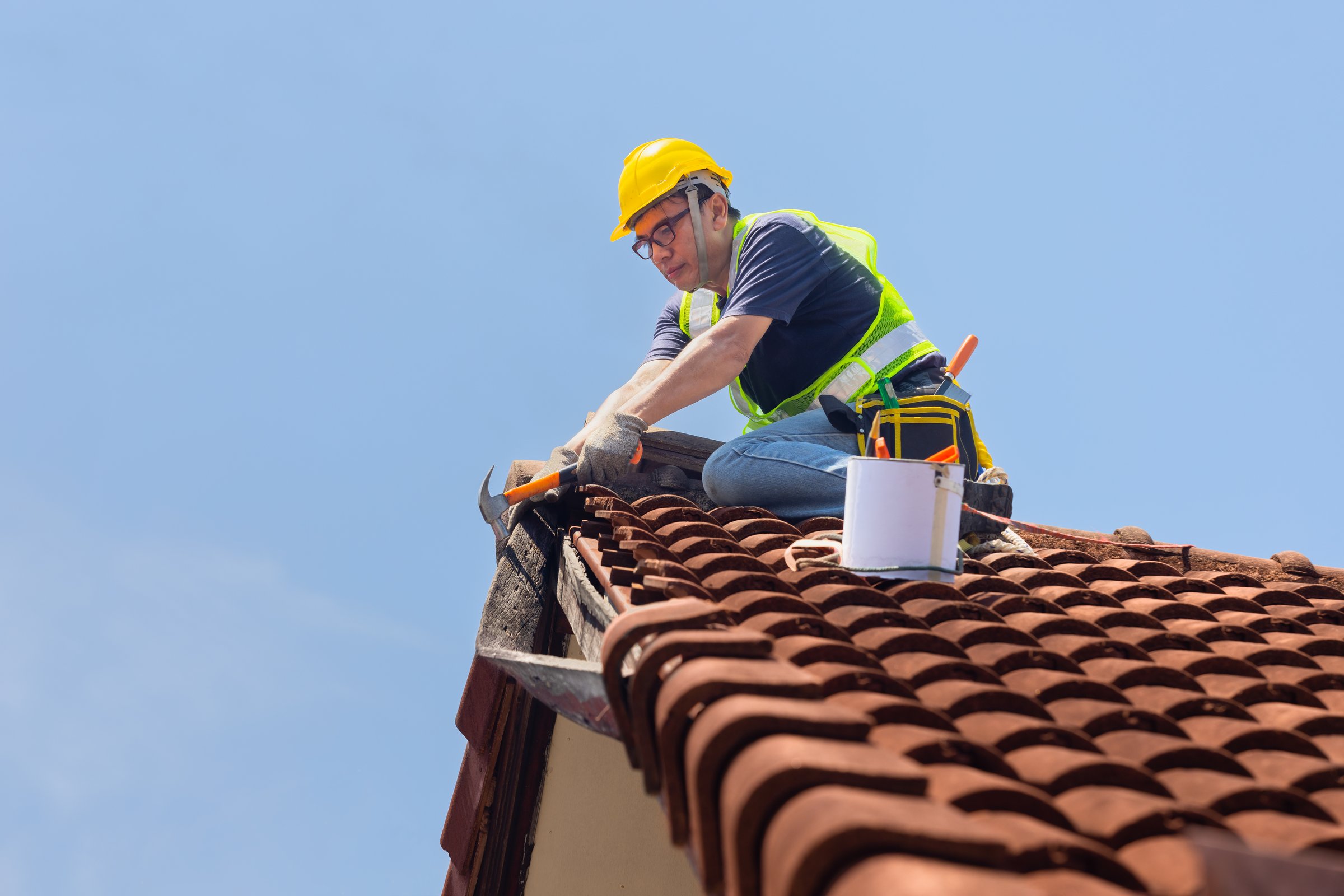 Worker man repairing eaves and tile of the old roof.