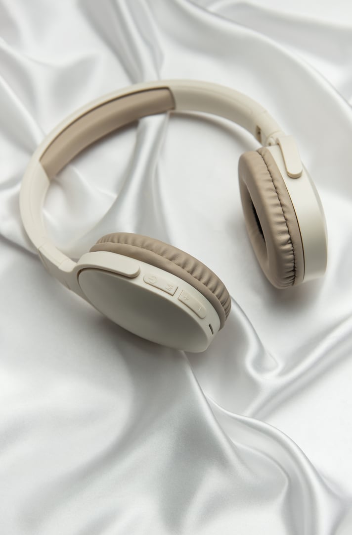 Beige and white wireless headphones resting on a luxurious white silk background, creating a sense of elegance and high quality audio experience