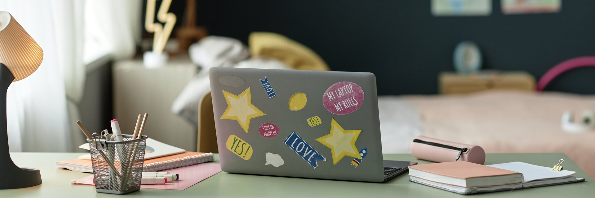 Header background image of open laptop decorated with stickers on desk in childs room with school supplies artistic workspace environment