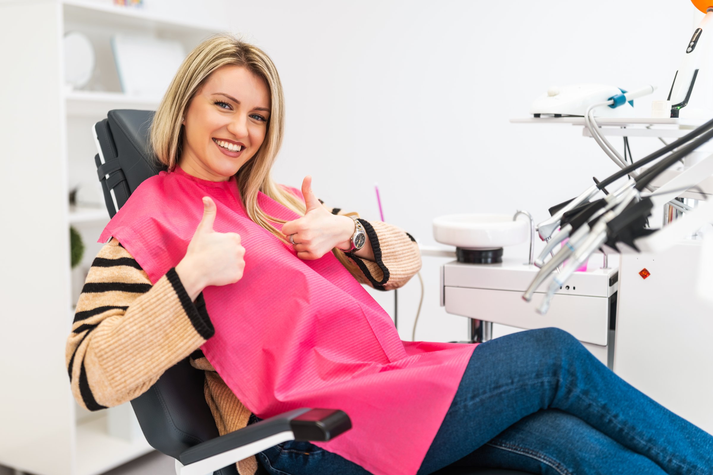 Happy young woman at dentist clinic. Professional dental care and hygiene. She is showing thumbs up.