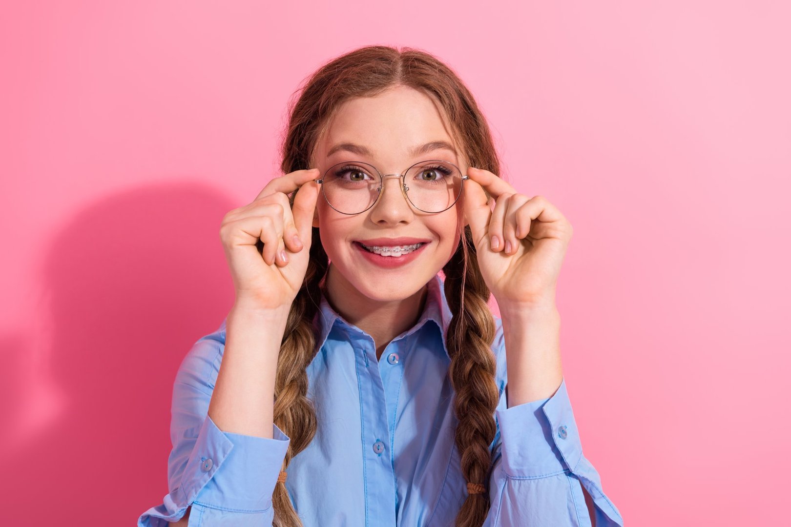 Excited student wearing glasses and braided hairstyle smiles confidently on a colorful background, embodying youthful joy and style
