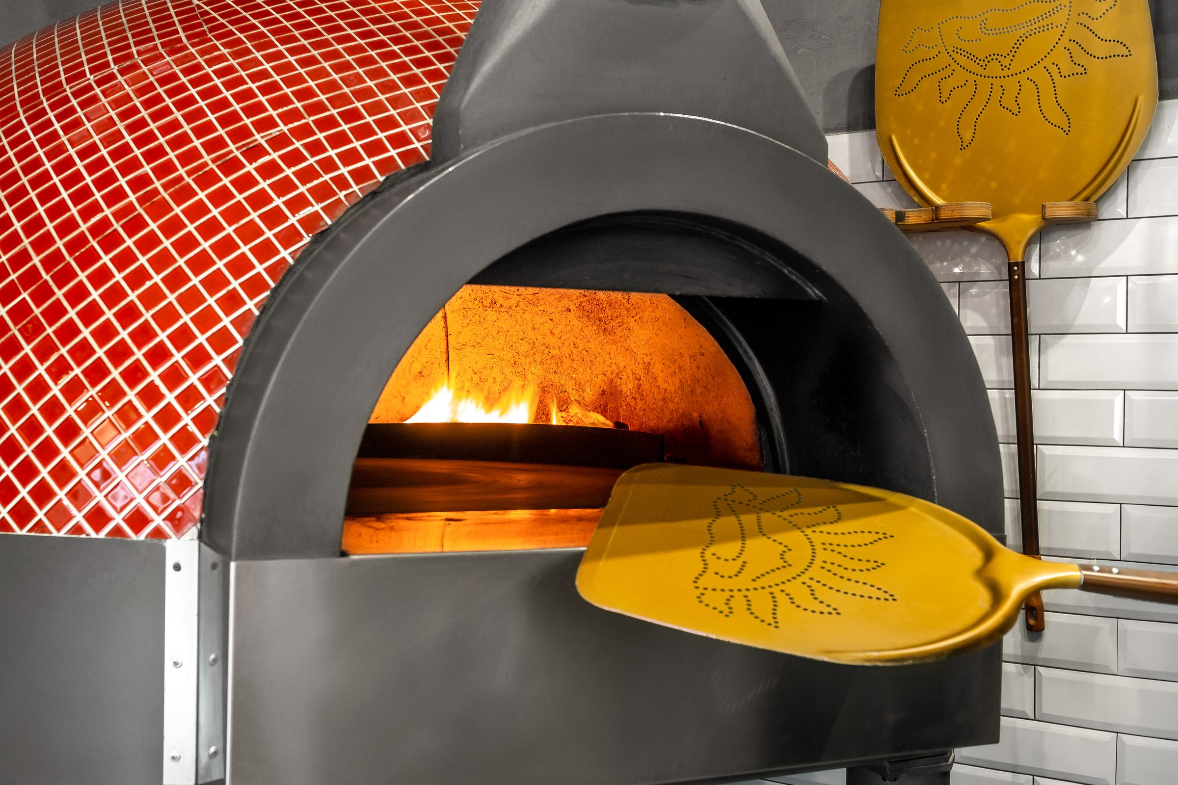 Traditional wood-fired pizza oven with open flame and yellow peel.