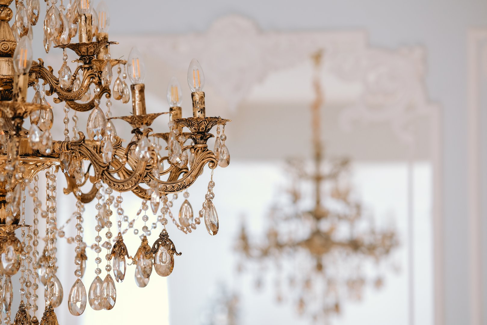 A stunning crystal chandelier hangs gracefully from the ceiling, casting a warm glow across a beautifully decorated space, highlighting its opulent design and intricate details.
