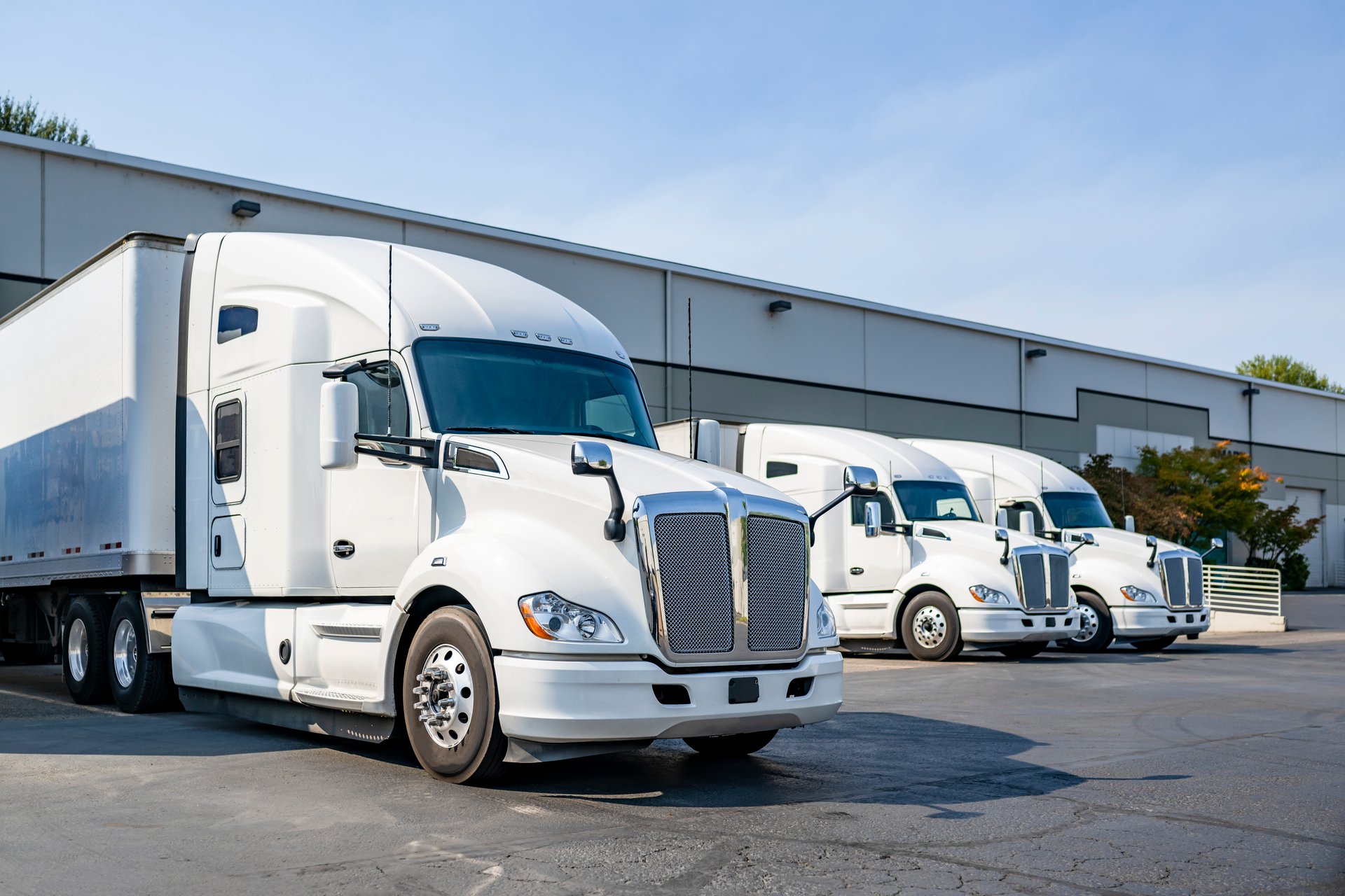 Industrial long hauler carriers white big rig semi trucks tractors with high cab for truck driver rest standing on the parking lot in warehouse docks gates loading cargo for the next delivery freight