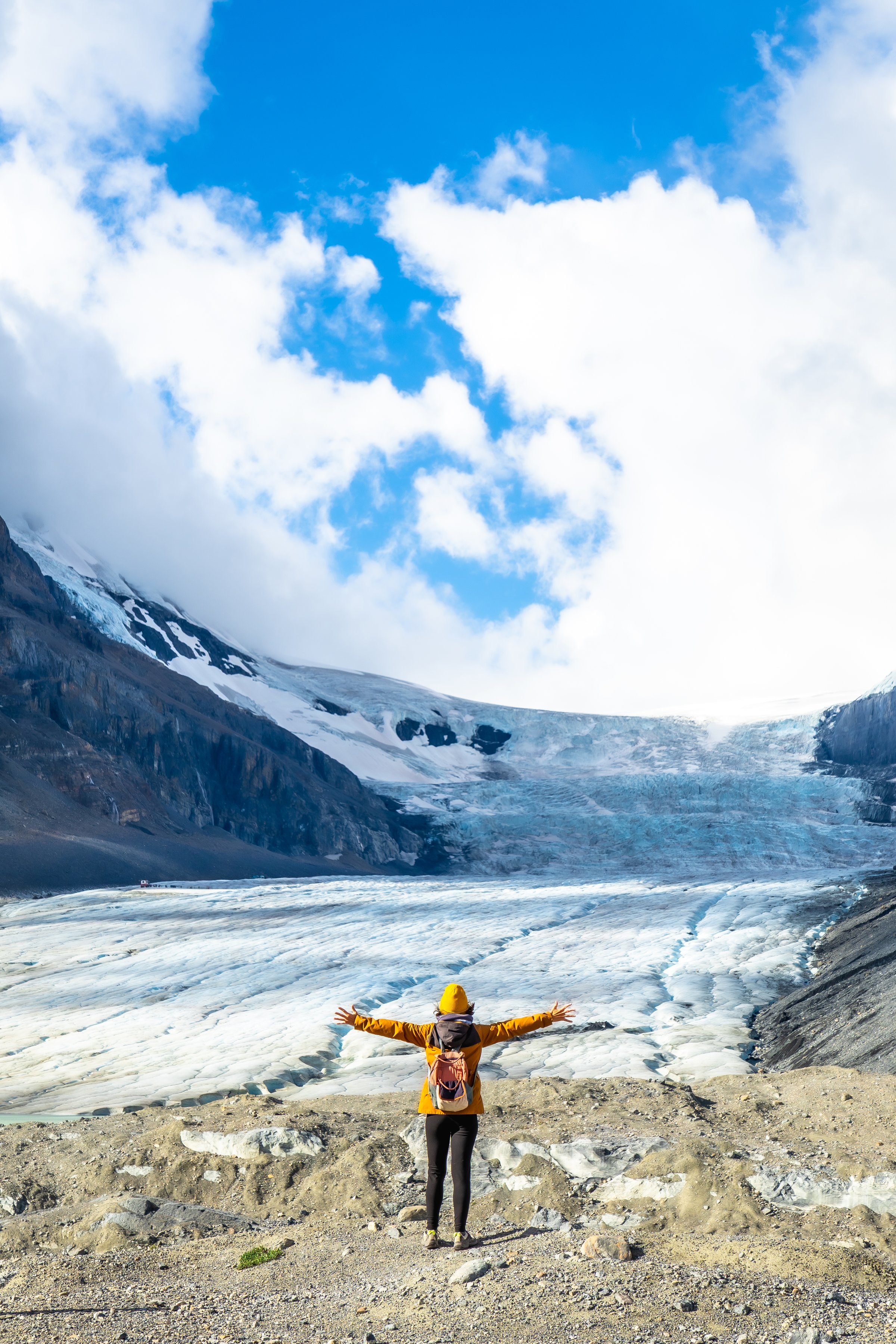 Young female hiker with open arms contemplating the stunning landscape of the athabasca glacier, a popular tourist destination in the canadian rockies, jasper national park, alberta, canada