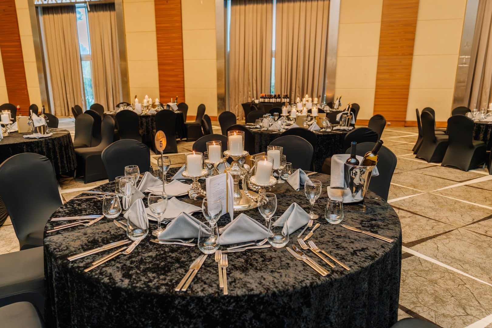 Turkey, Belek - February 28, 2025 - Luxurious banquet hall setup with round tables, candle centerpieces, wine bottles, and elegant place settings prepared for a formal dinner event.