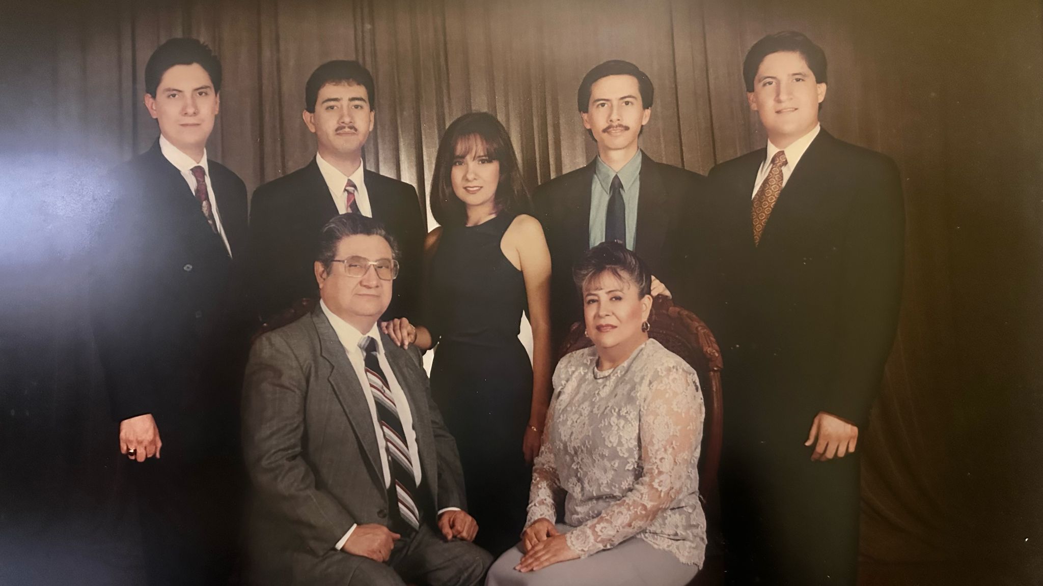 A formal family portrait with five men, one woman, and an older couple seated in front, all dressed in suits and dresses.