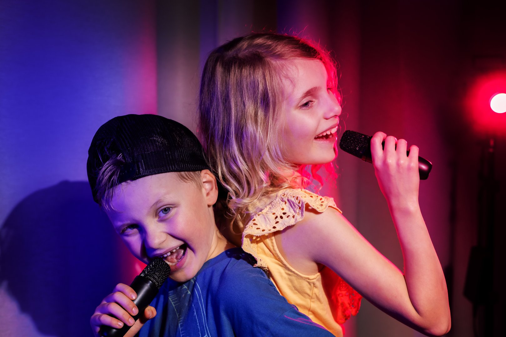 Happy boy and girl duet sing in microphones. karaoke party, children concert performance. neon lights