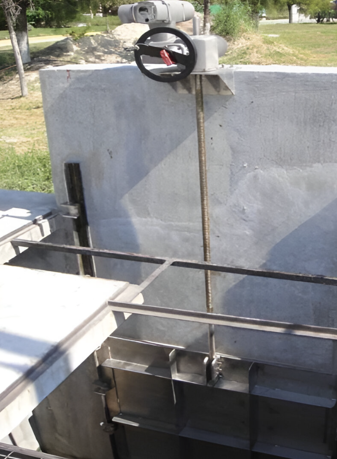 A metal valve control mechanism on a concrete wall, part of a water control system in an industrial or infrastructural setting.