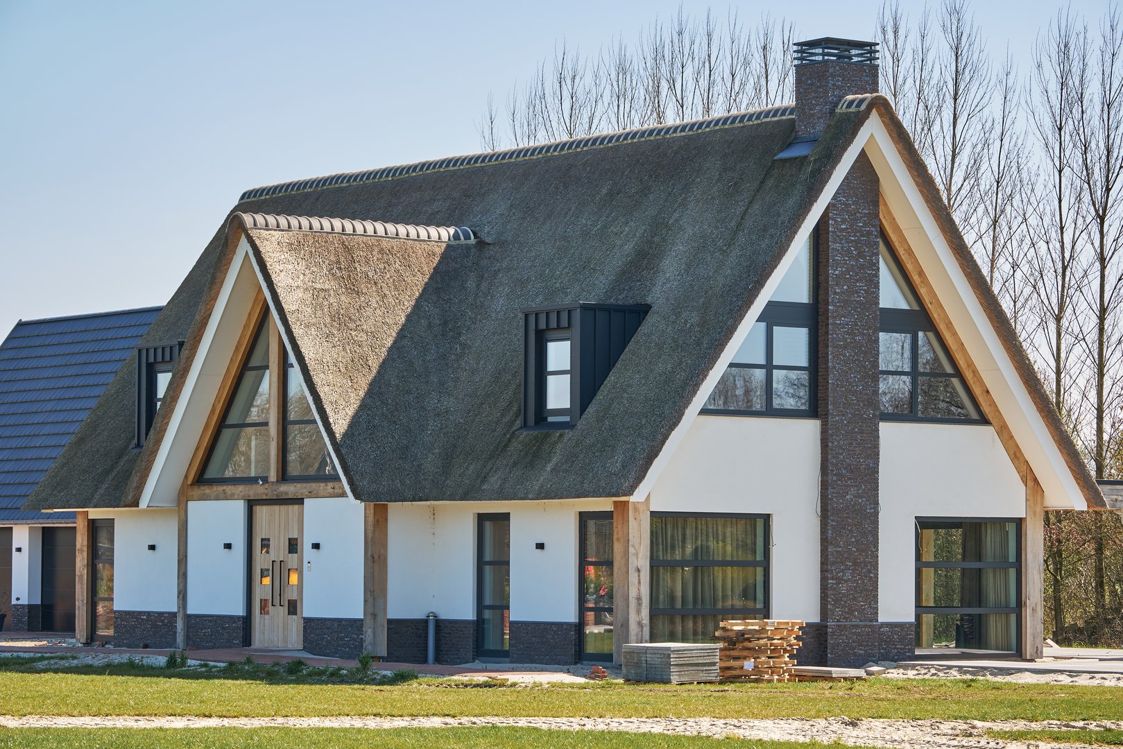 April 1, 2025 - Nieuweroord-Netherlands: Newly built modern villa with a thatched roof on a spacious plot, construction materials still visible, just completed.