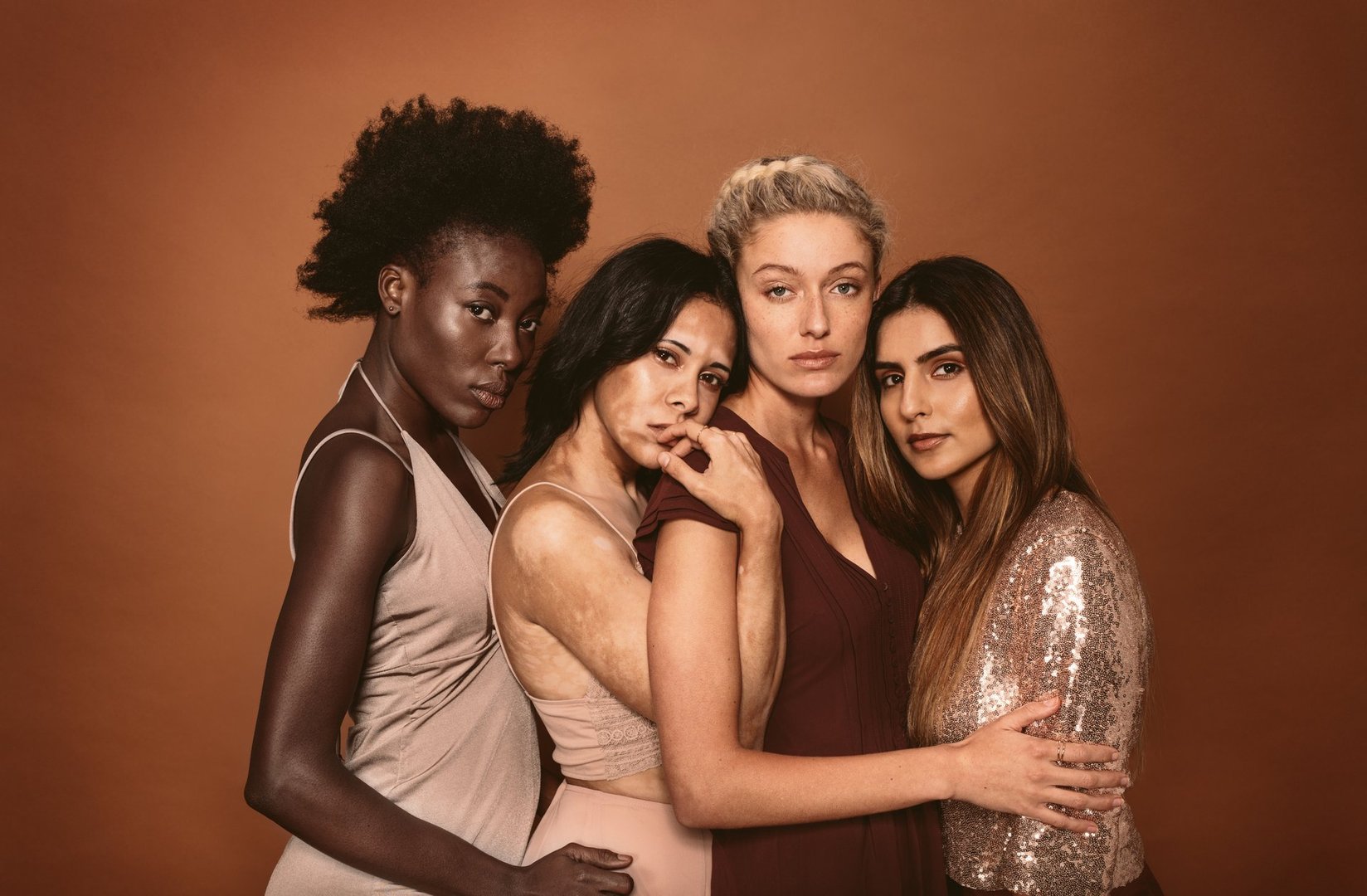 Portrait of stylish young women standing over brown background. Multi ethnic fashion models posing together in studio.