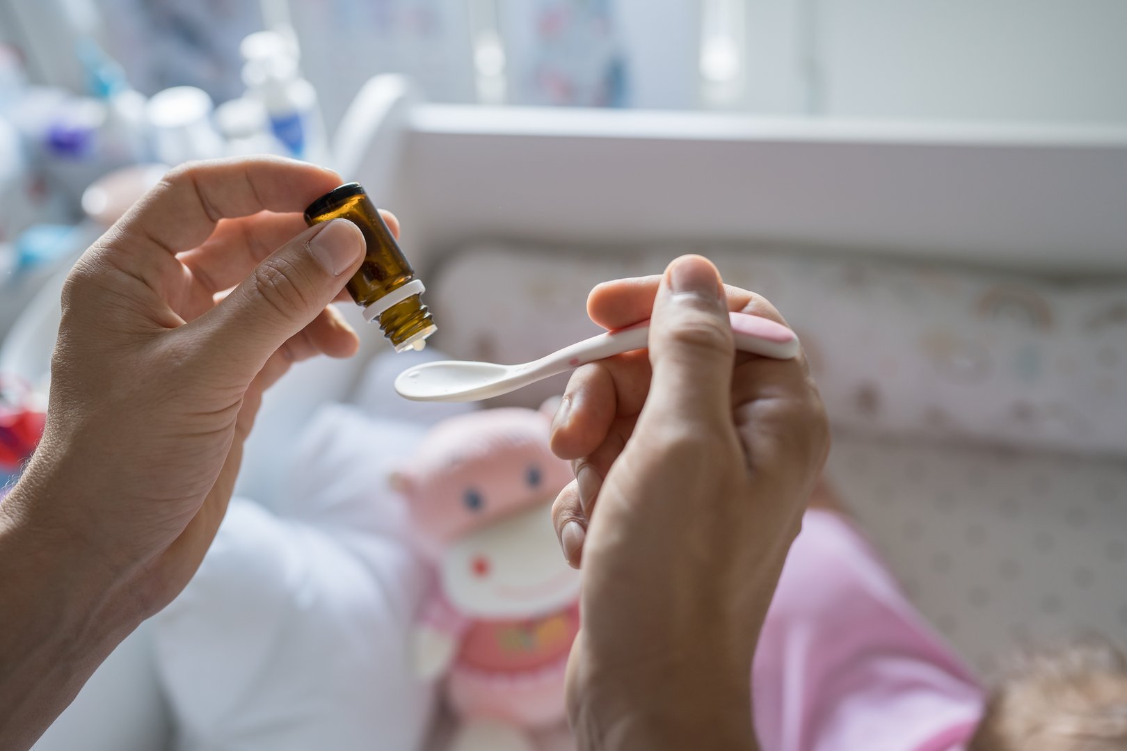 Father preparing spoon with probiotic drops medicine for his small caucasian baby girl while standing by the cradle crib at home close up on hands selective focus copy space care and parenting concept