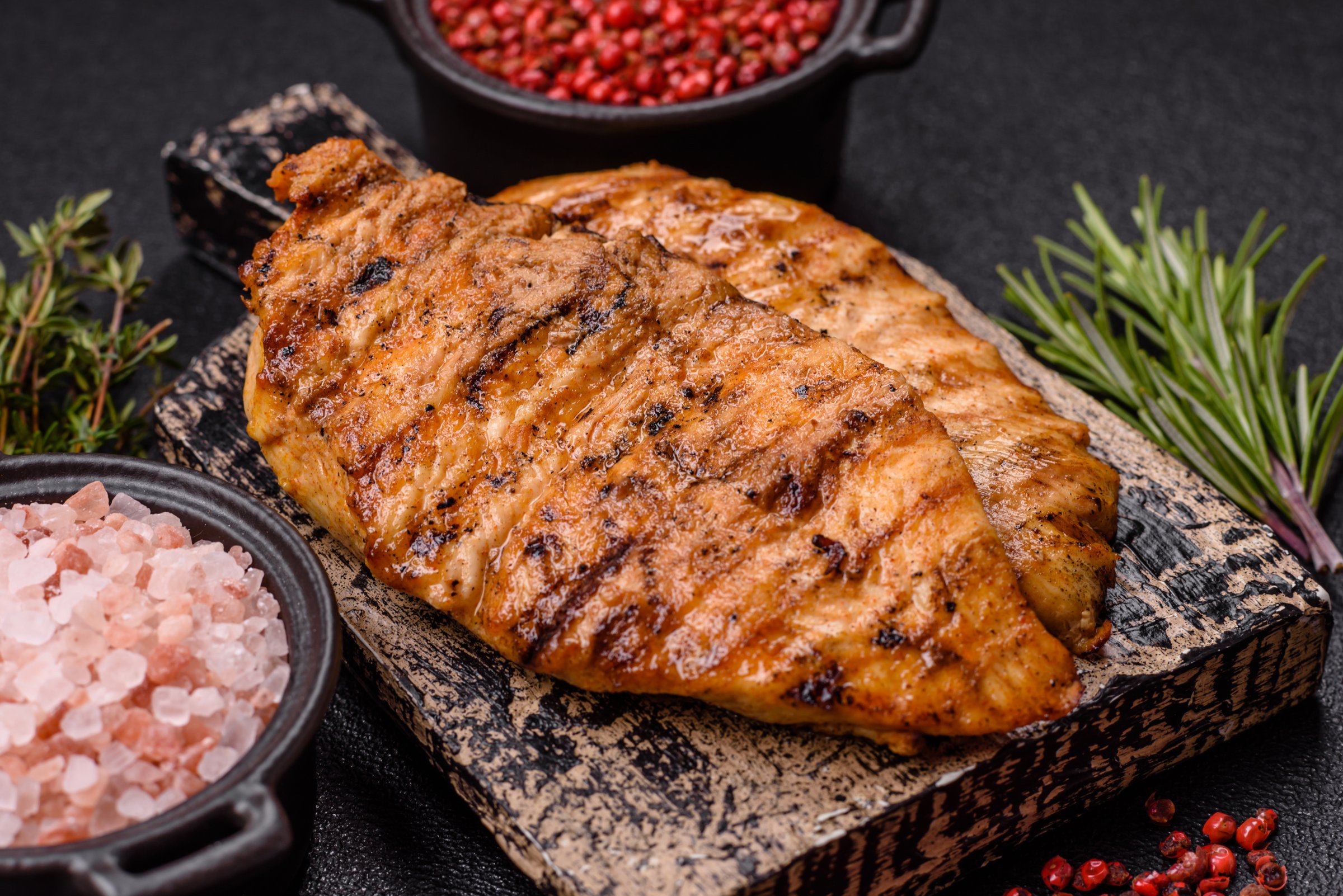 Delicious fresh grilled chicken fillet with spices and herbs on a dark concrete background. A dish cooked over fire