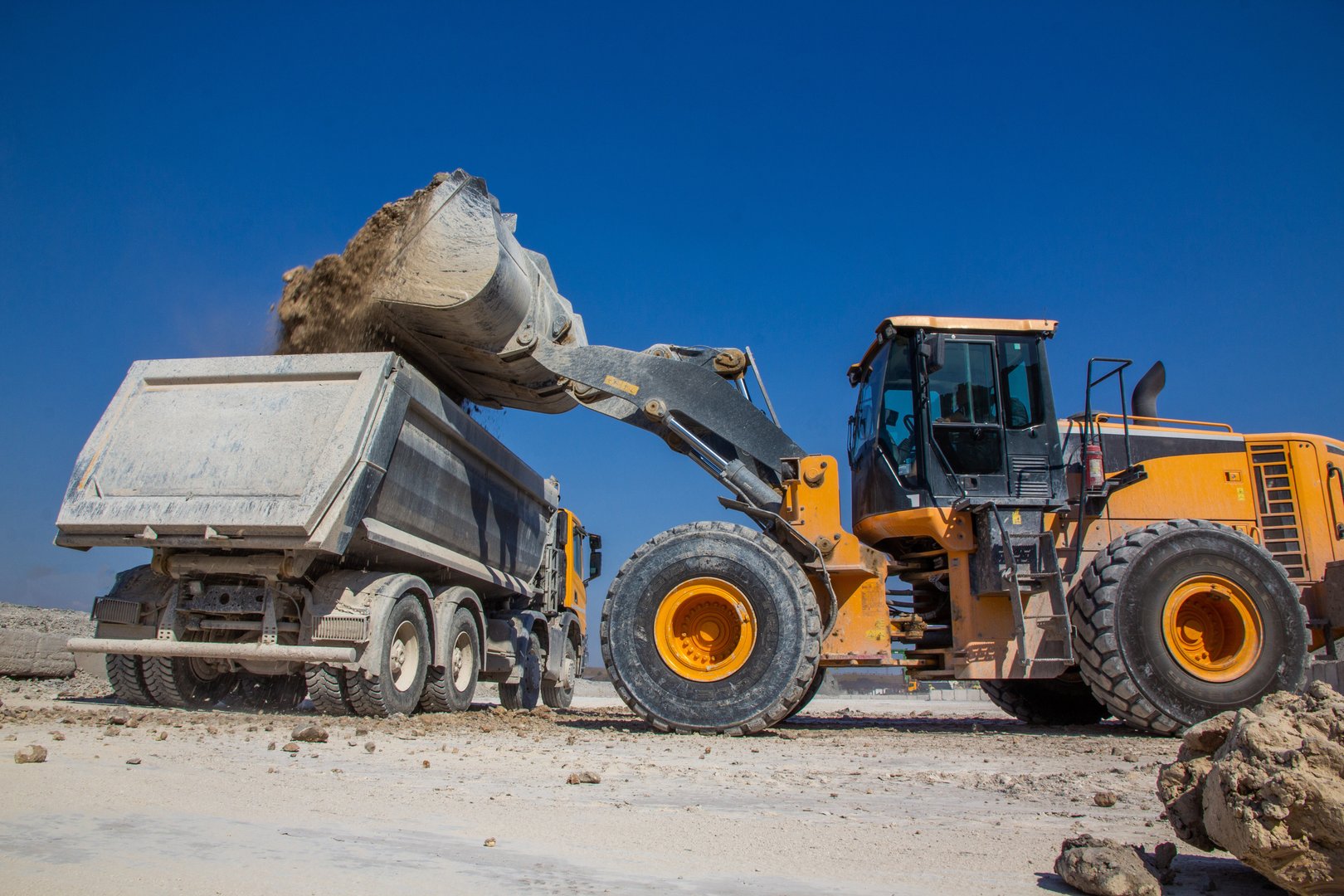 a bucket loader pours soil into the body of a large dump truck