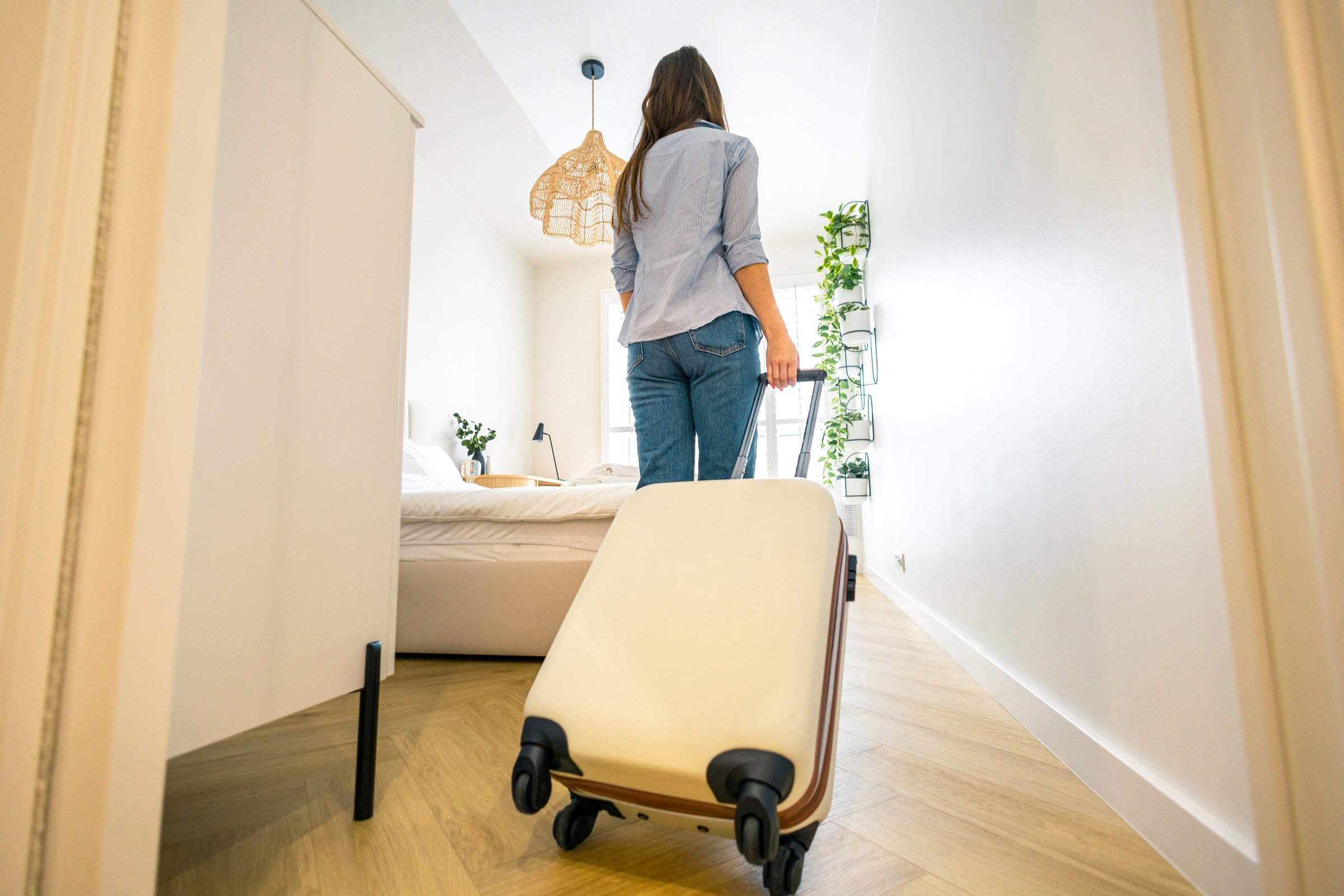 Rear view of a young woman entering a hotel room with her luggage