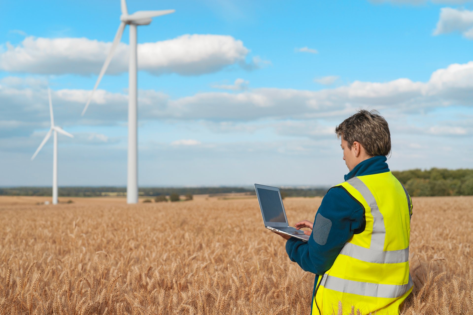 Engineer conducts field with laptop research in field near wind turbines making notes