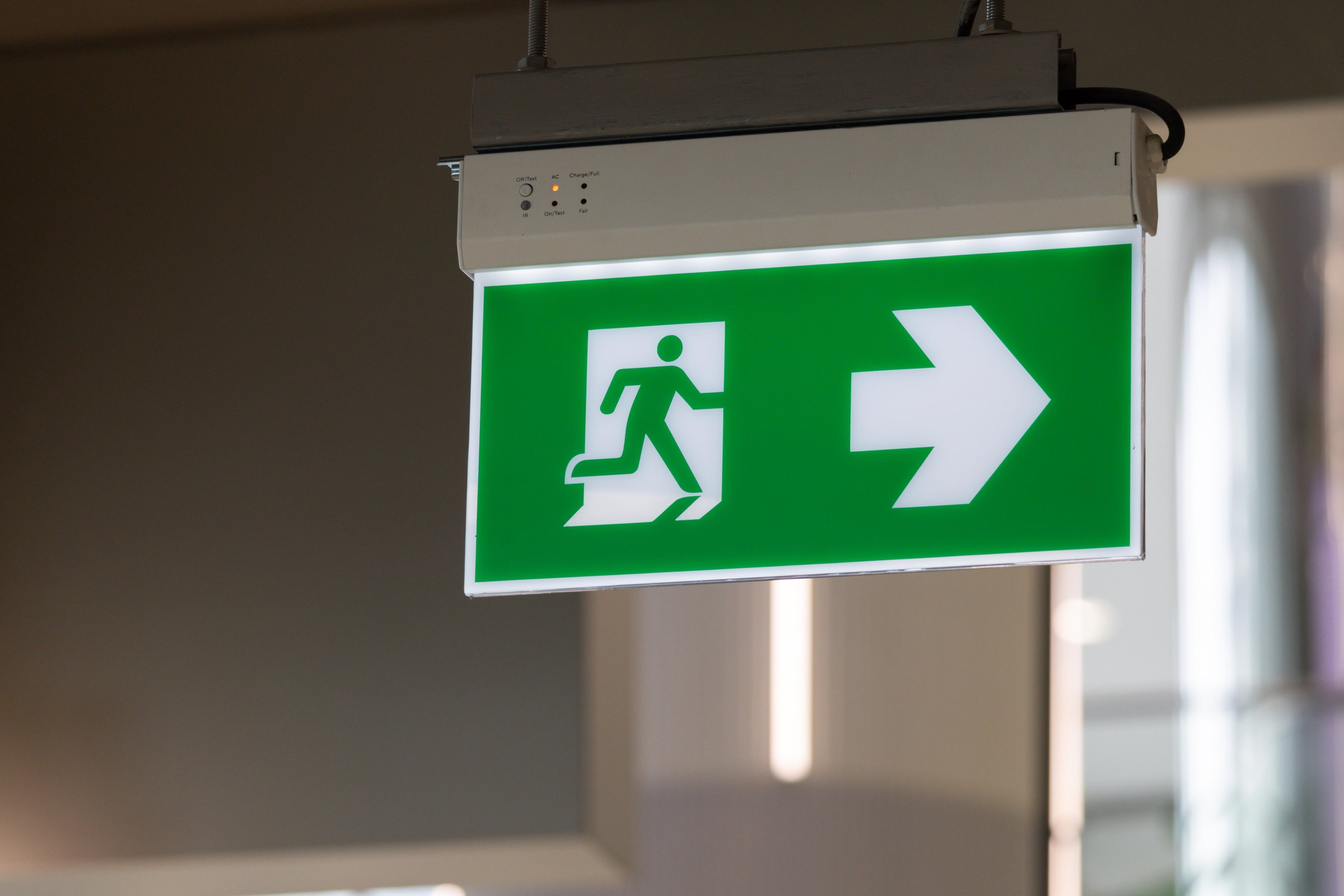 A green sign with a running man and an arrow pointing to the right. The sign is hanging from the ceiling