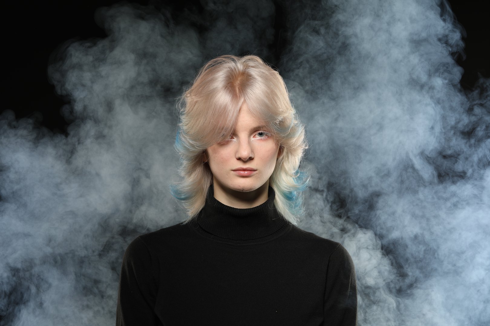 Beautiful young woman with stylish short haircut and colored hair dyeing blue hair. Close-up portrait over black and smoked background.