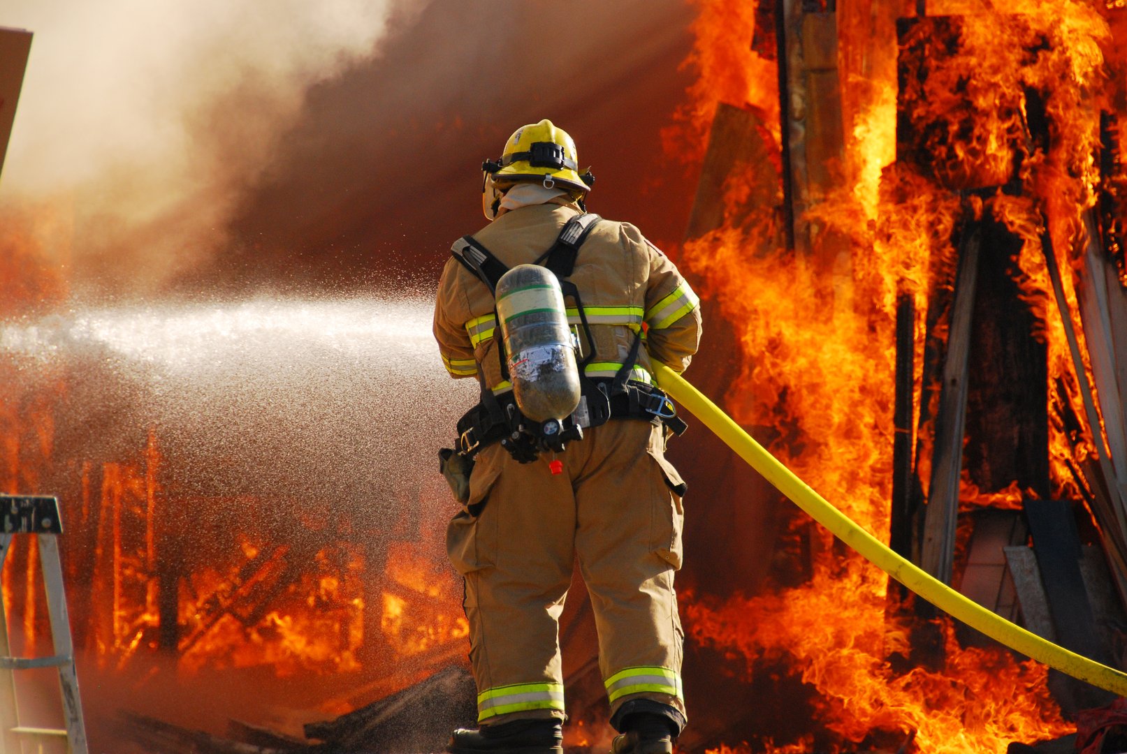 Single fire fighter spraying a straight steam into a fully involved shop fire