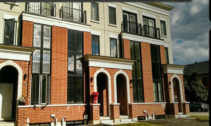 Modern townhouse with red brick exterior, large windows, and arched doorways against a cloudy sky.