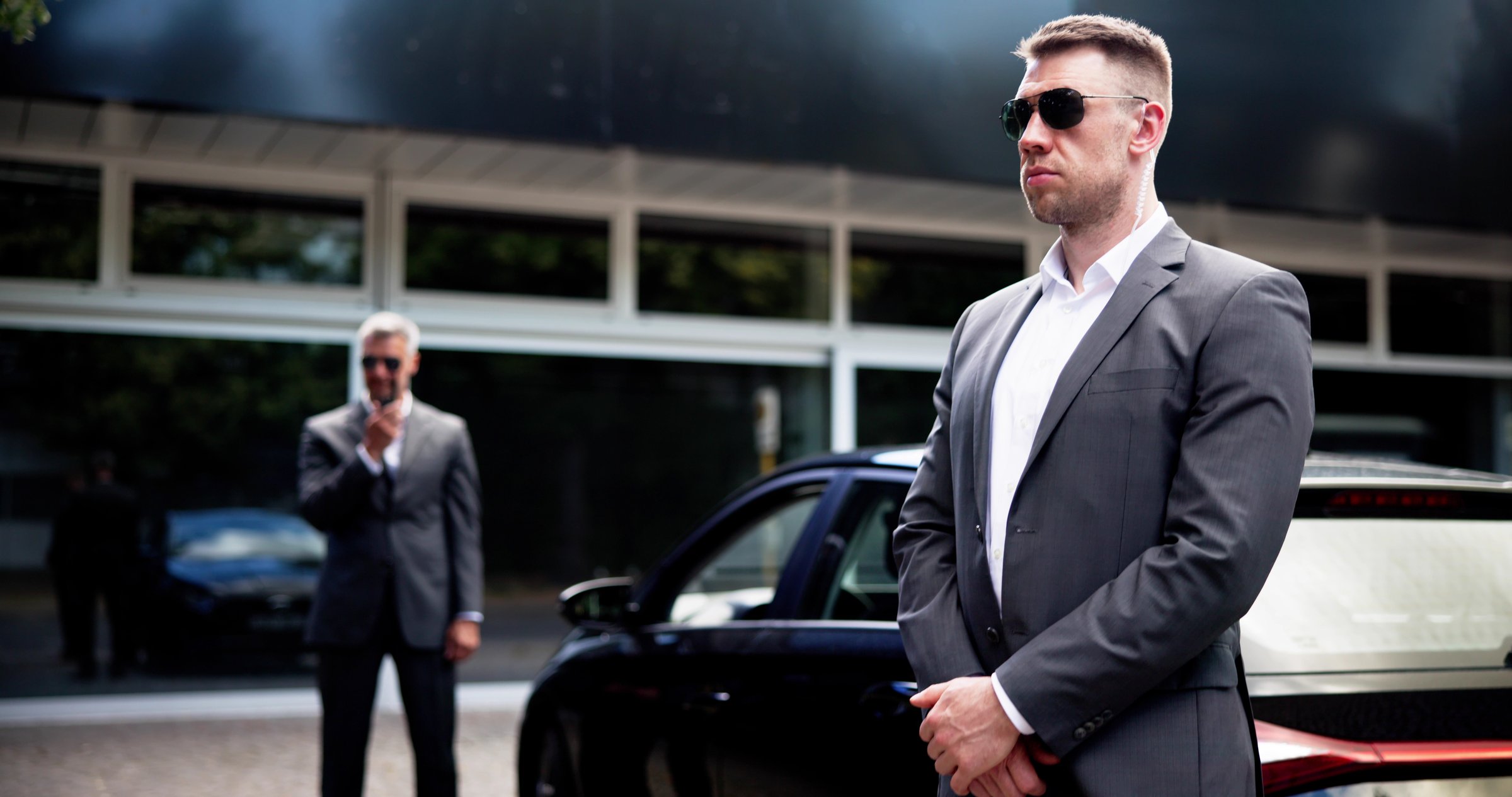 Corporate Executive Protected by Professional Security Guard Near High-End Luxury Car in VIP Setting for Client Safety.