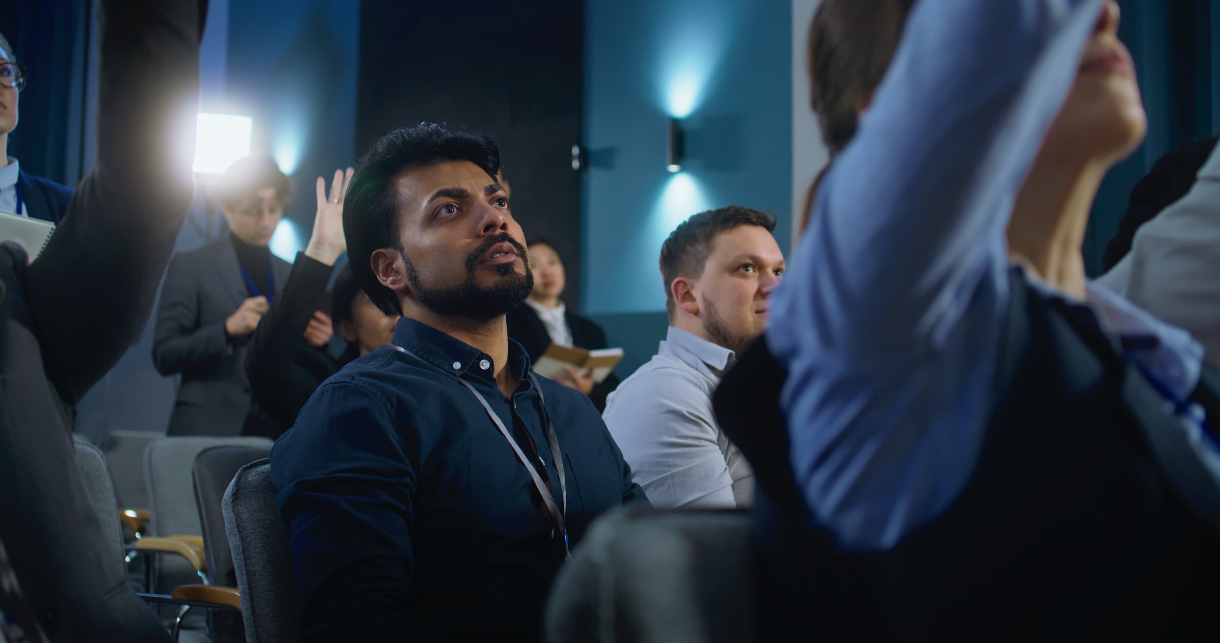 Indian male media representative raises hand and asks question during press campaign with activist, businessman or politician. Multiethnic journalists sit in conference room of government building.