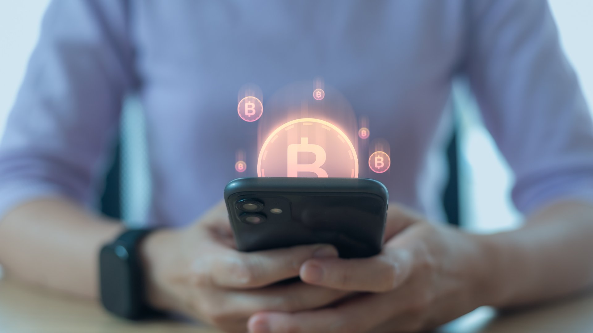 Hand holding smartphone with bitcoin hologram, concept of cryptocurrency, blockchain technology, mobile wallet, digital payment, fintech innovation, and online investment in modern finance.