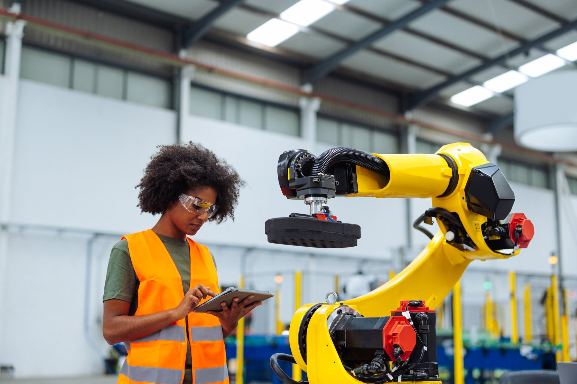Industrial engineer using digital tablet programming robotic arm in modern factory