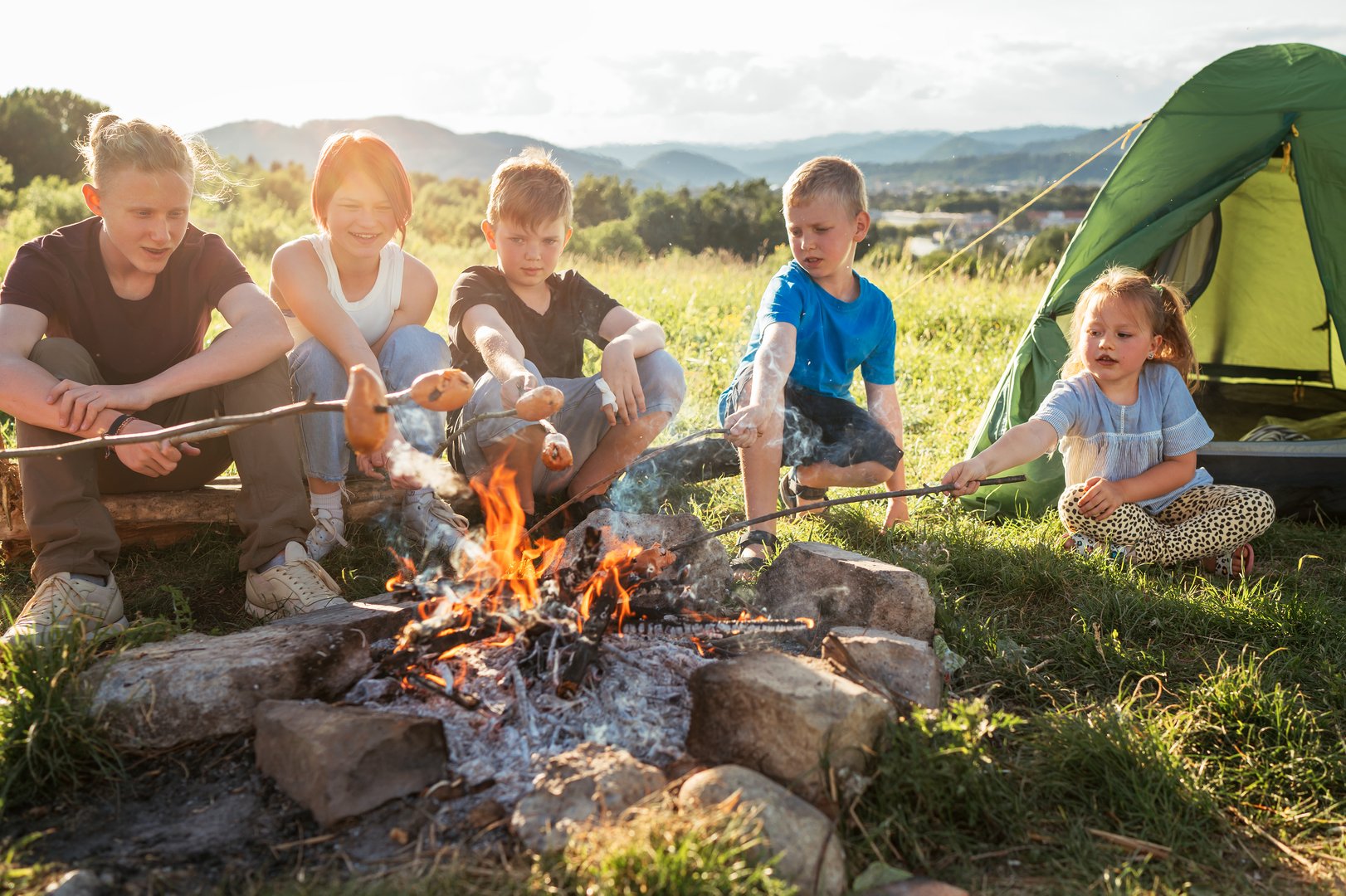 Kids roasting sausages over campfire in nature