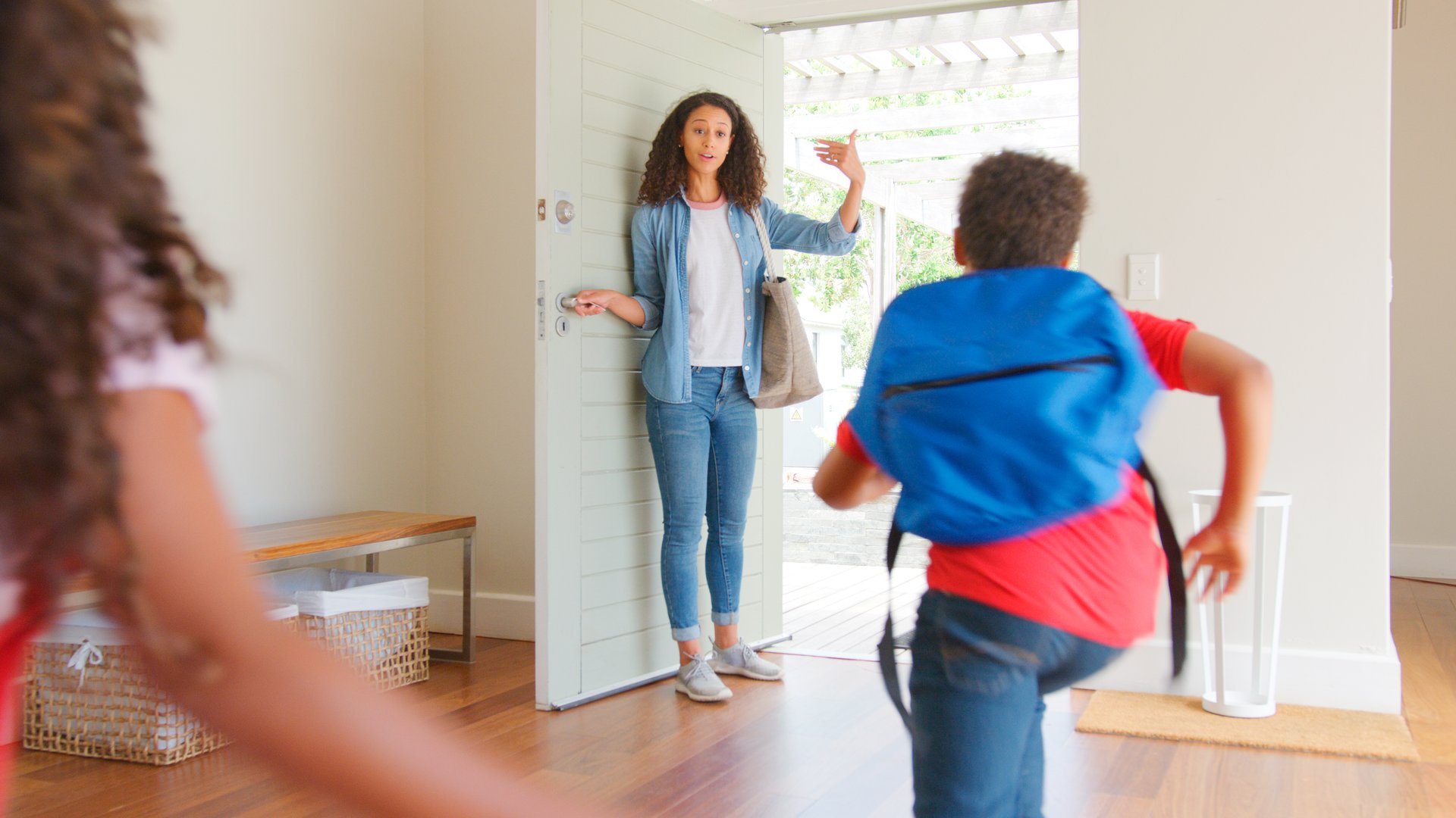Mother Standing At Front Door Encouraging Children Ready To Leave House For School