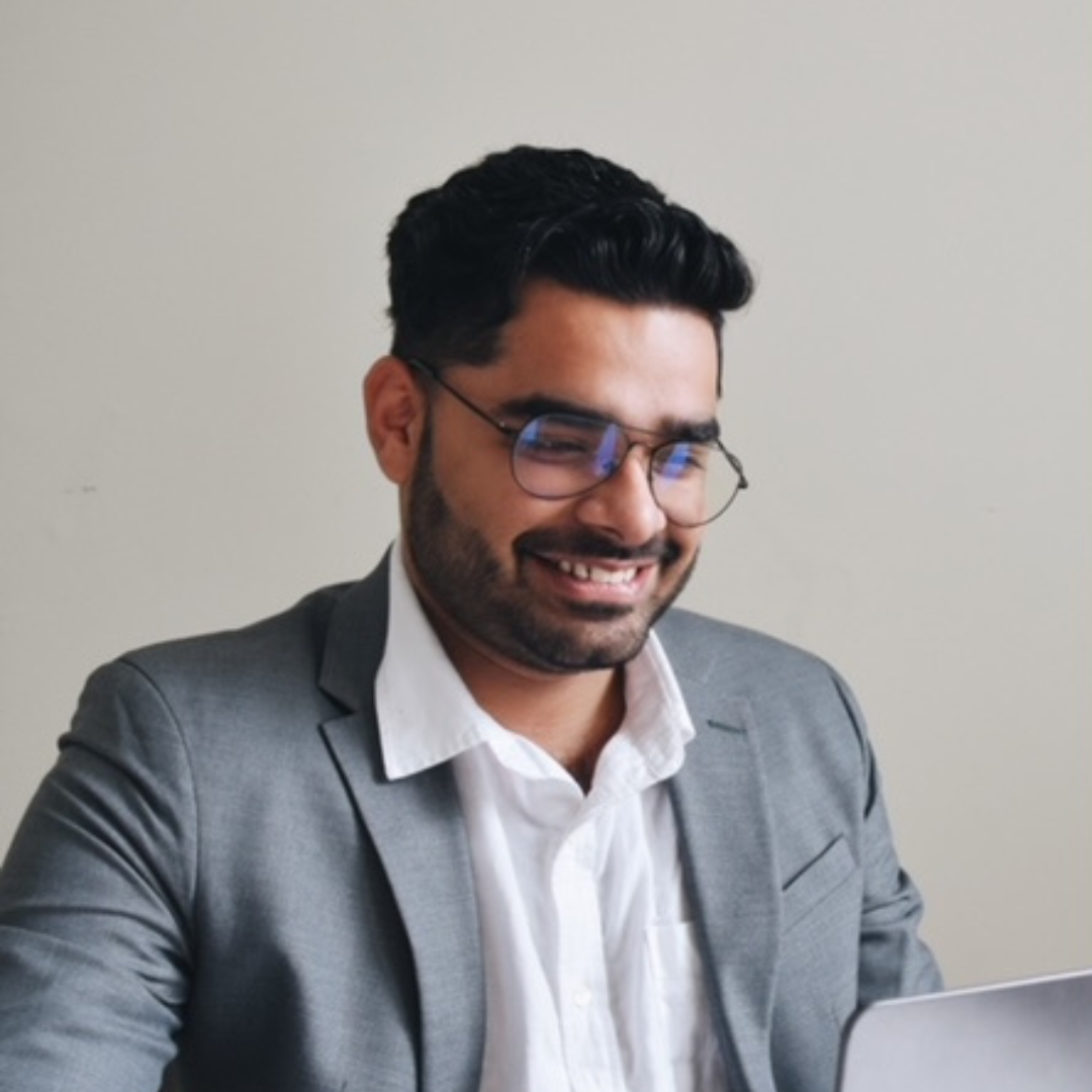 Man in a gray suit smiling while looking at a laptop.