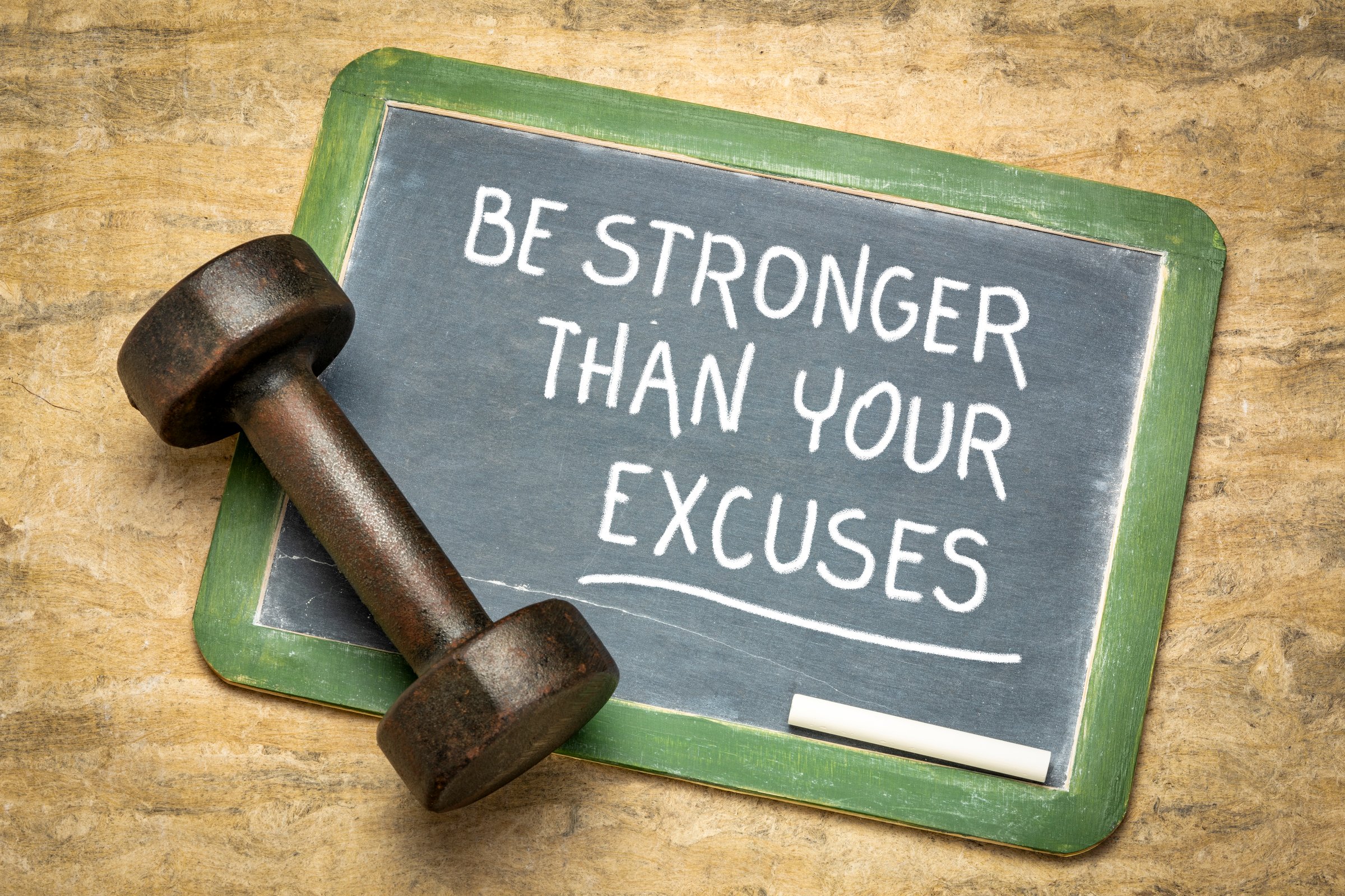Be stronger than your excuses - fitness motivation quote on a slate blackboard with an iron dumbbell