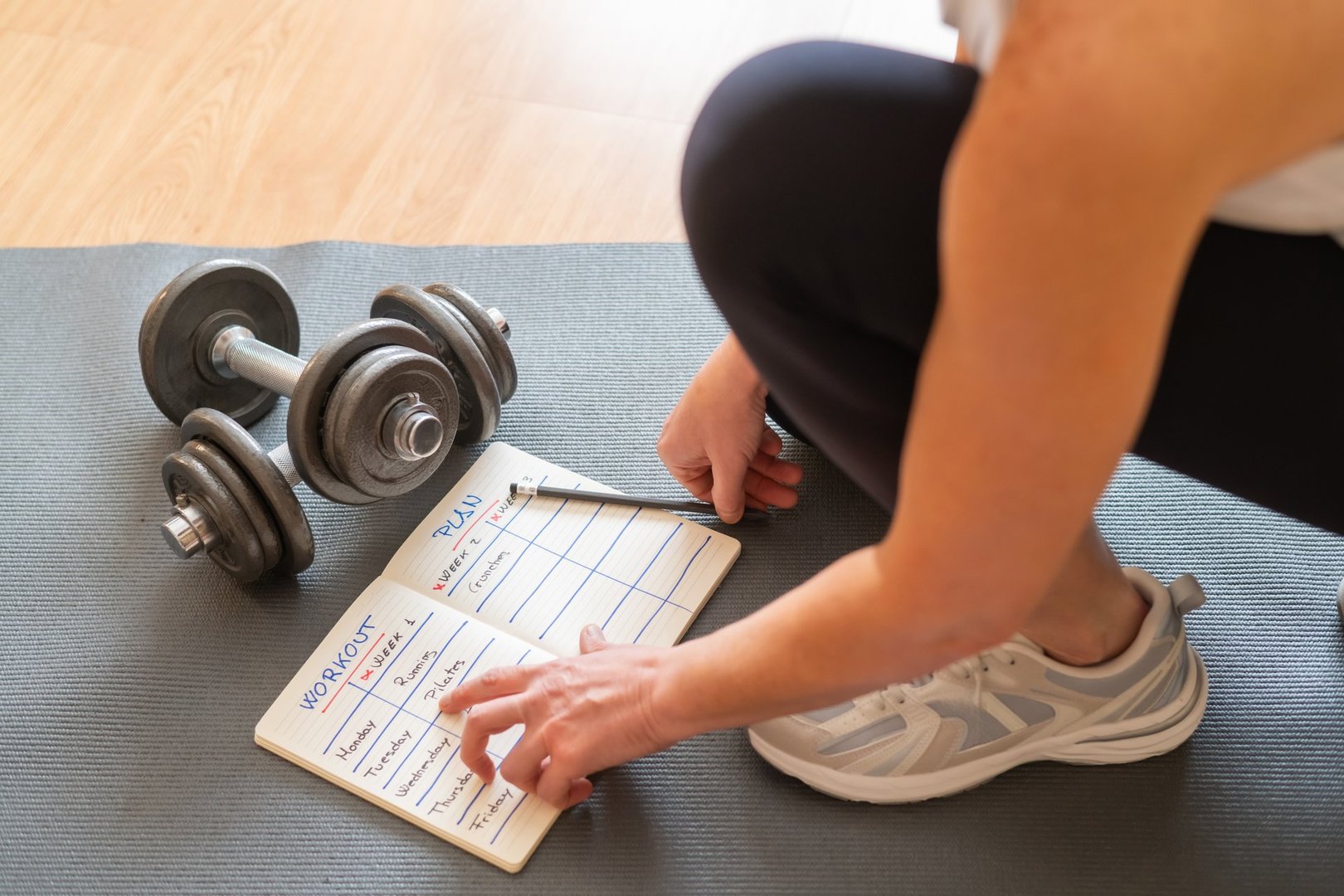 Female Athlete Organizing Fitness Plan On Notepad While Sitting On Yoga Mat With Dumbbells, Creating Healthy Daily And Weekly Exercise Routines, Promoting Active Lifestyle Goals, Morning Motivation - High Performance Nutrition for Athletes 35+ at SugarFree.Space